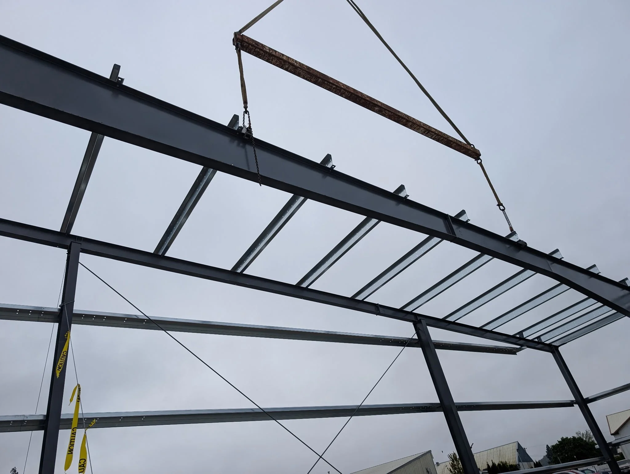 Construction site scaffolding with metal beams and rusted crossbar against an overcast sky, caution tape hanging from one beam.
