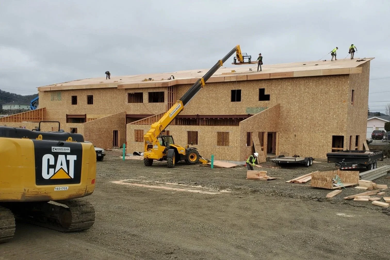 Multi-story commercial building under construction with roofing installation and heavy equipment.jpg