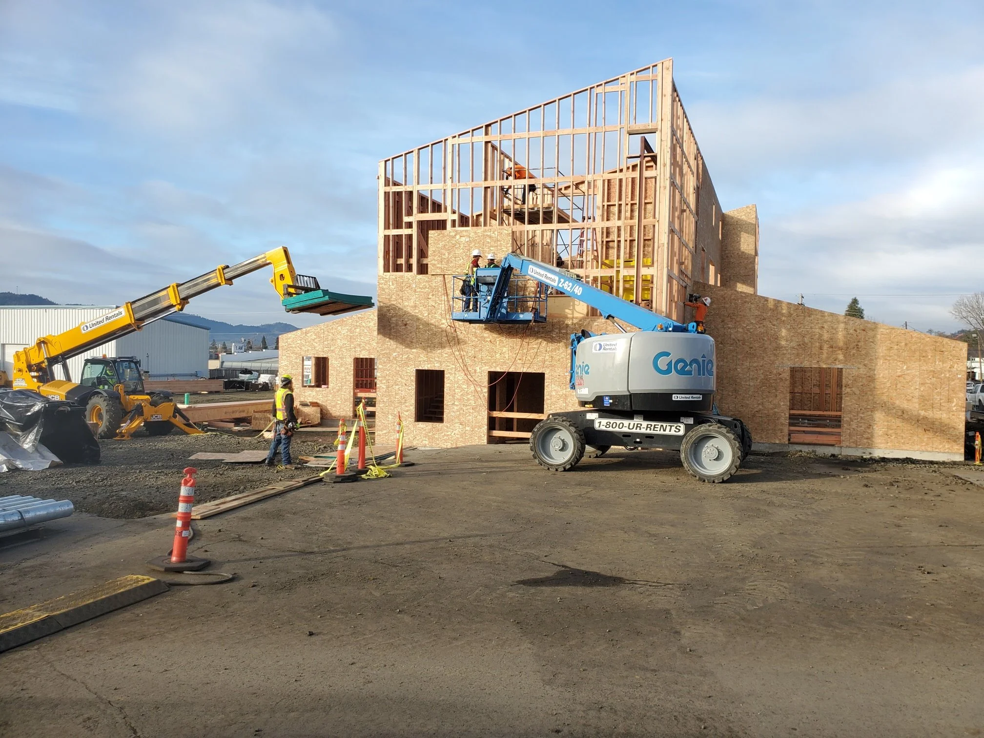Construction site with a wooden building framework, cranes, and construction workers wearing safety helmets.