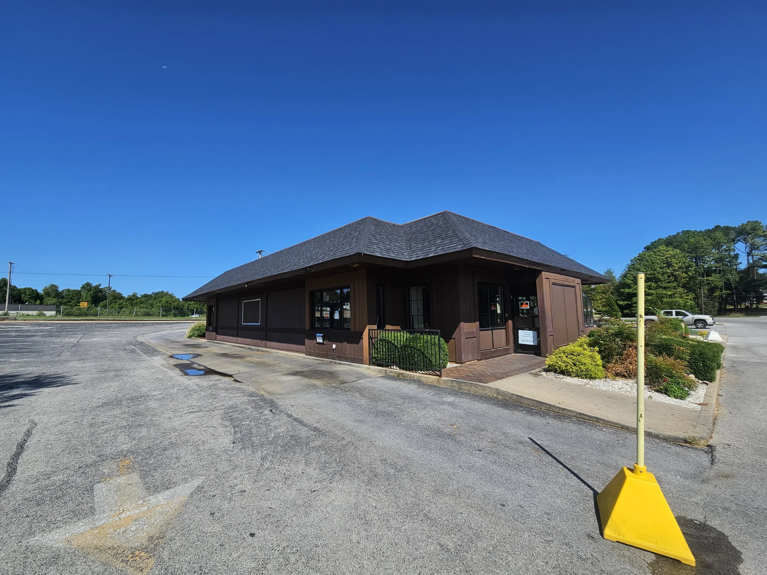 Standalone commercial building with updated exterior finishes, customer parking access, and landscaped entryway under clear blue skies
