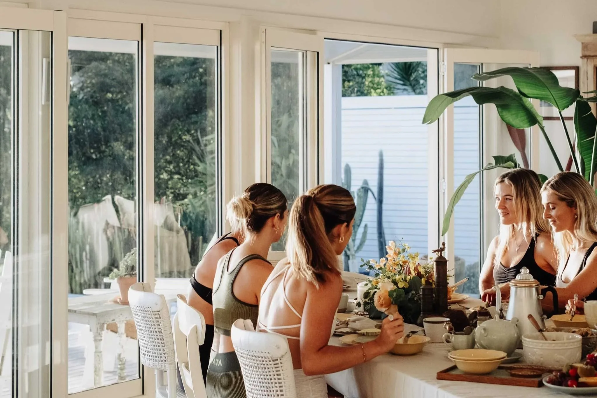 A group of women sitting around a table inside a bright room with large windows, having a meal together.