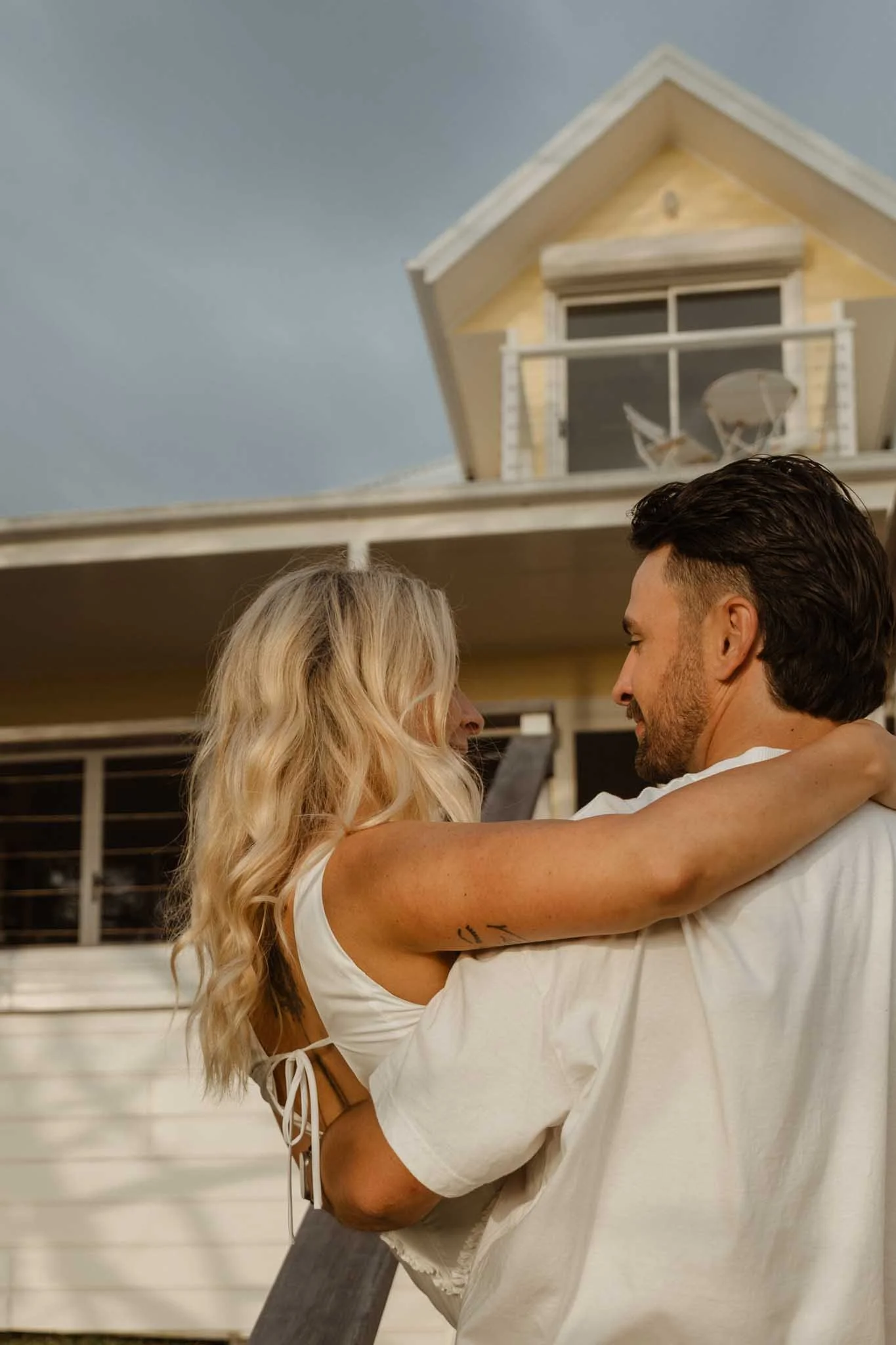 A couple sharing a romantic embrace on a balcony, with a house in the background.