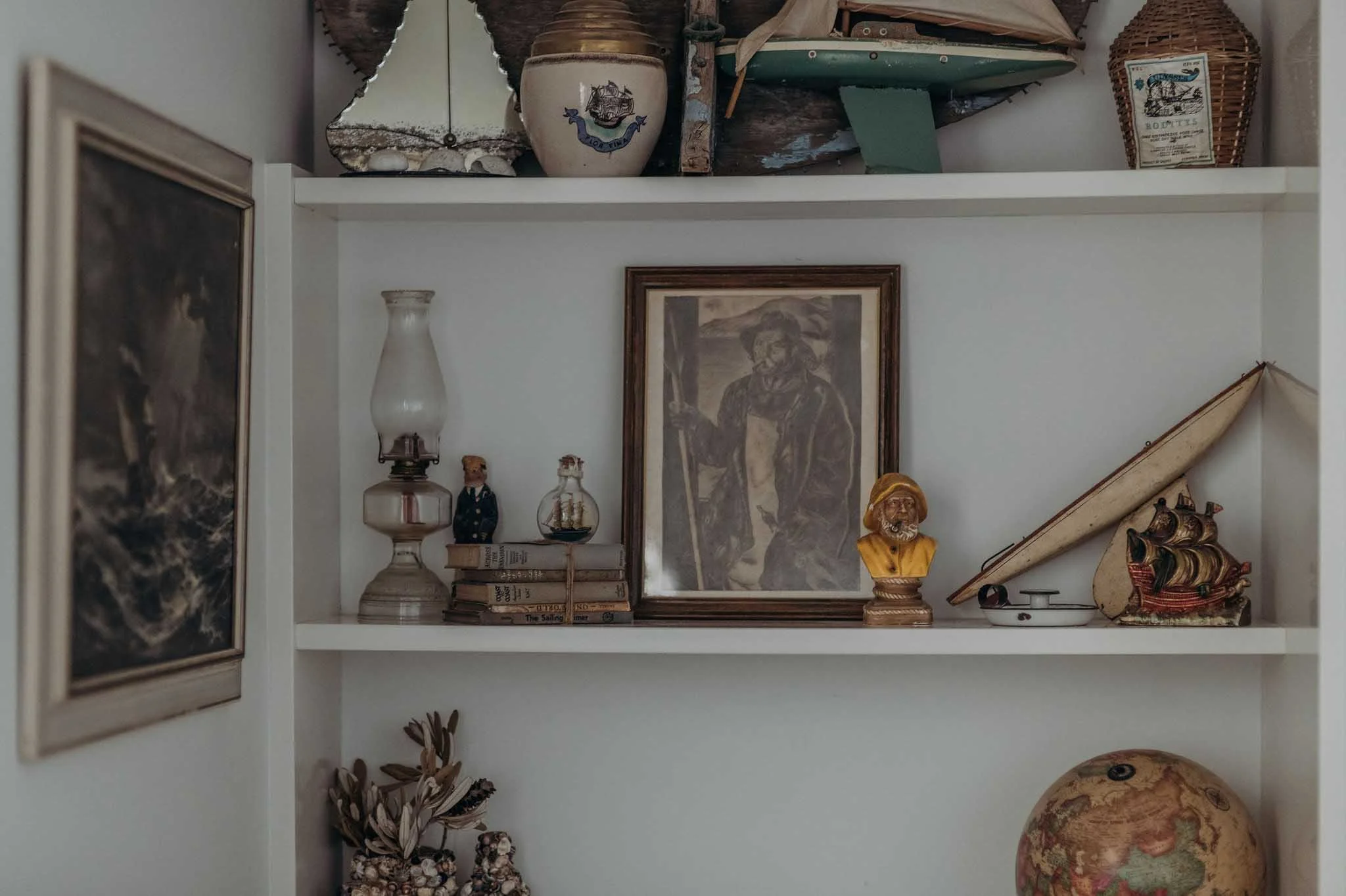 A bookshelf with various decorative objects, including a framed sketch, small bottles, a ceramic bust, a statue, and vintage books.