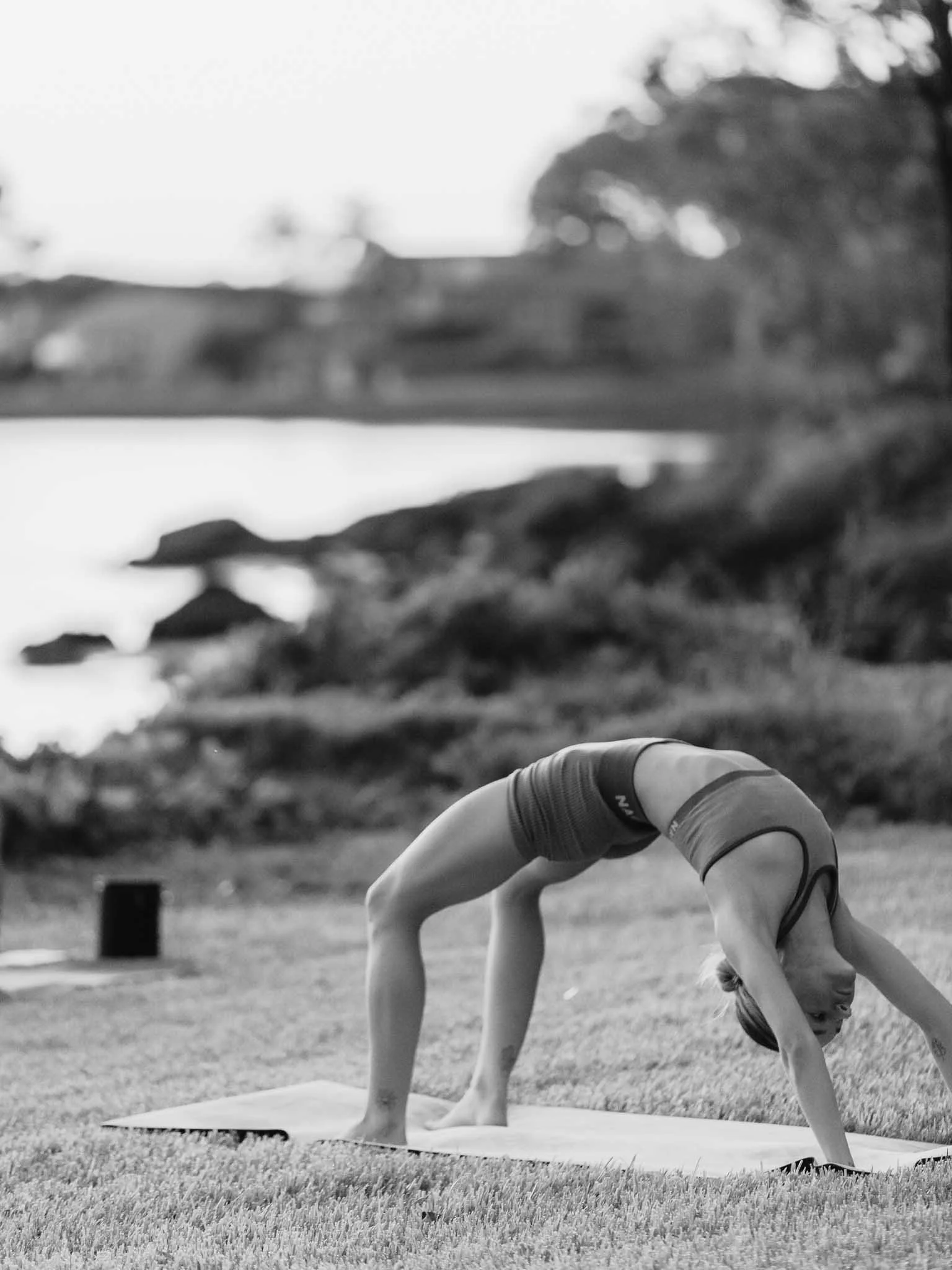 A person performing a yoga pose outdoors on grass, with trees and a cloudy sky in the background.