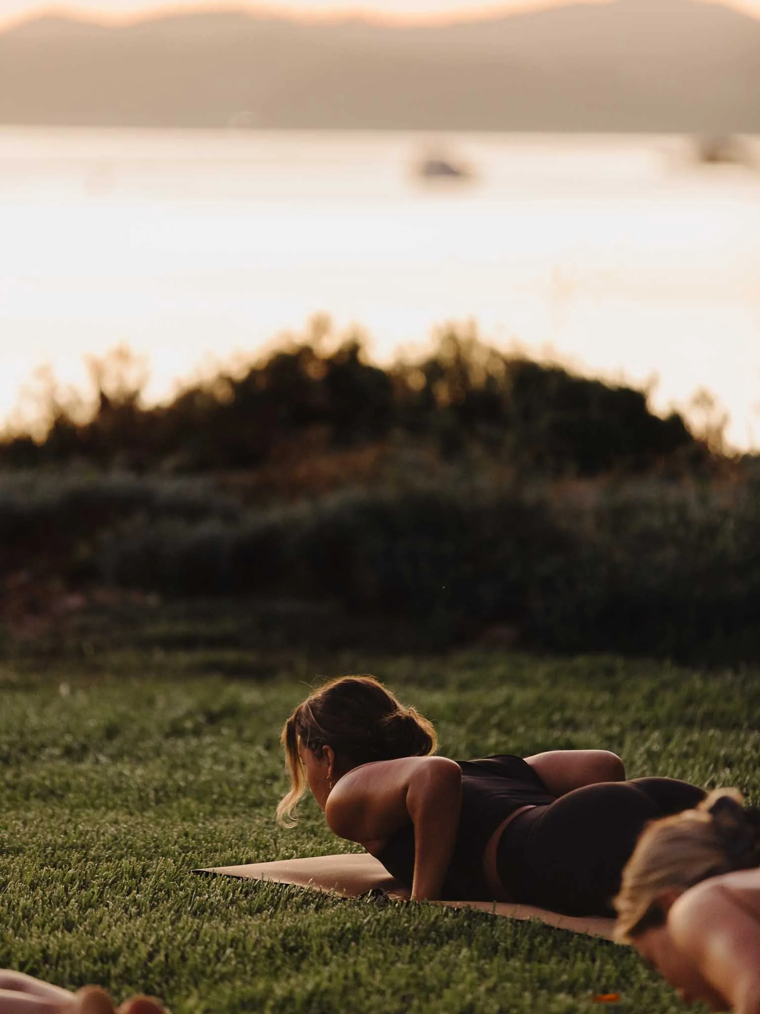A person doing yoga on a mat outdoors on grass during sunset.
