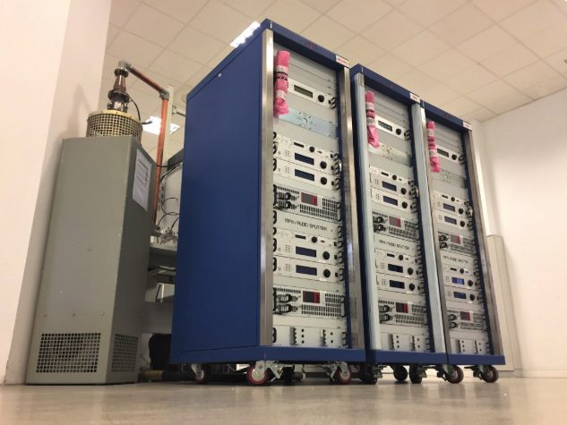 Three server racks with electronic equipment and control panels, situated on wheels in a server room.