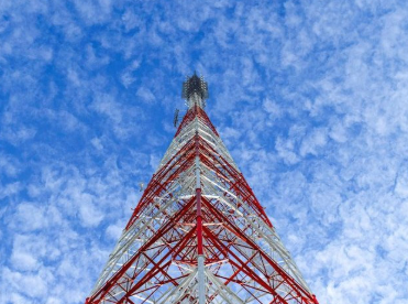 A tall telecommunications tower with a red and white lattice structure reaching into a blue sky with clouds.