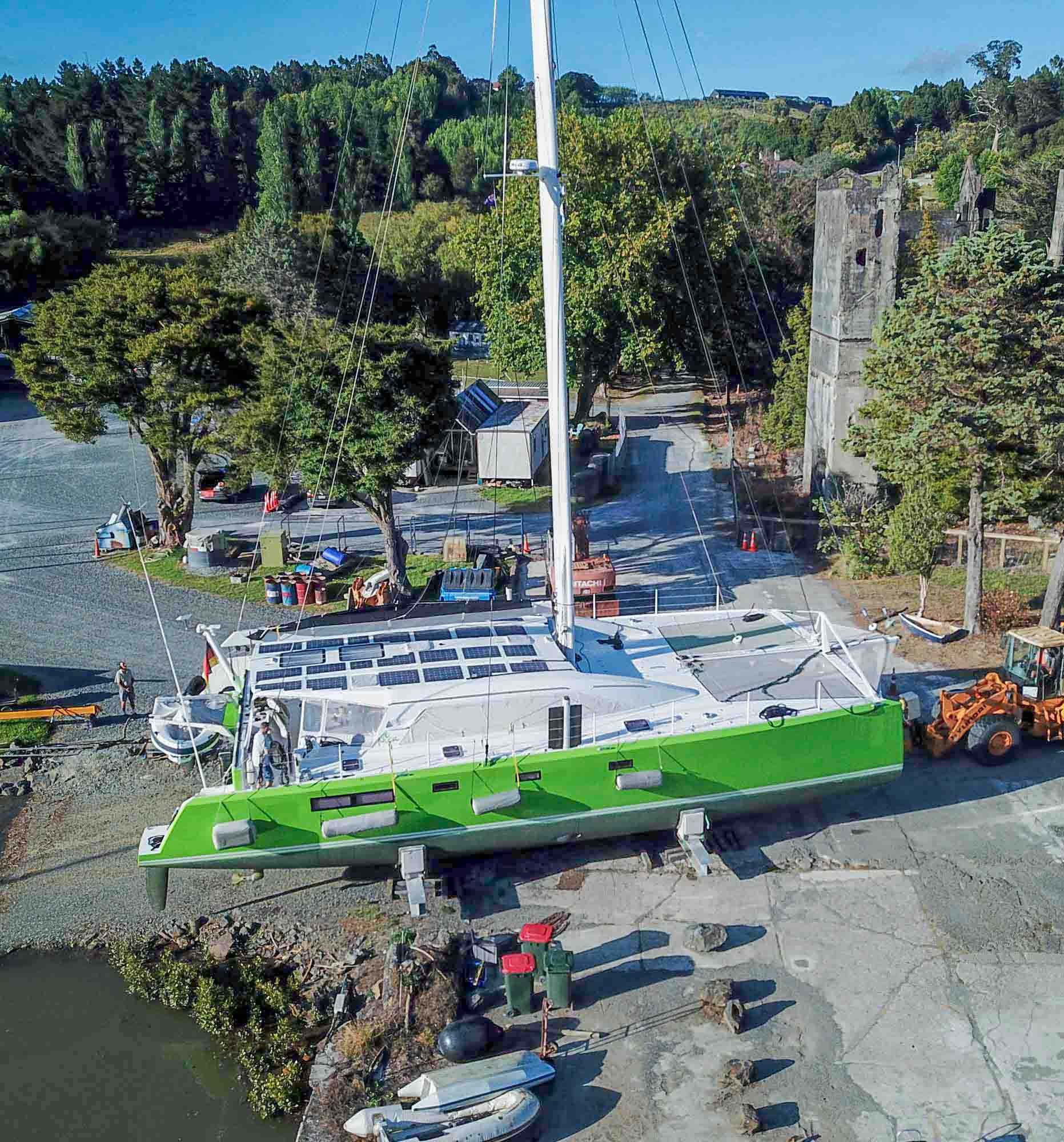 A green and white sailboat docked on land next to a pond, surrounded by trees and construction equipment.