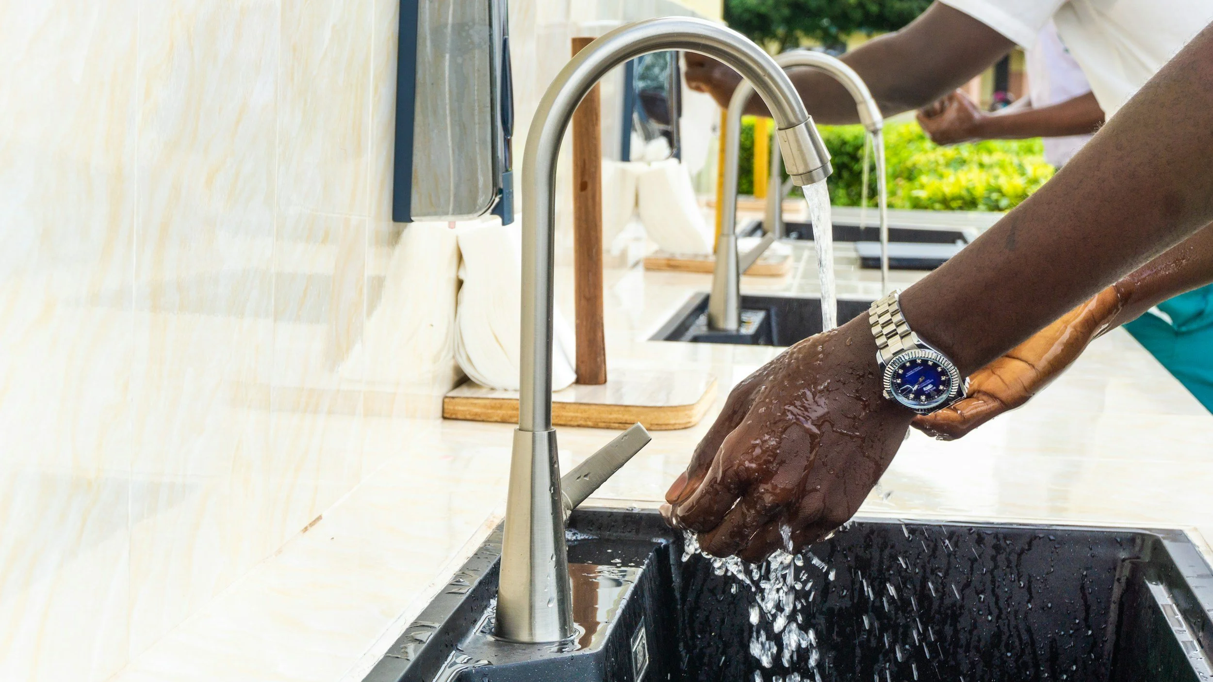 Person washing arms under a kitchen faucet outdoors.