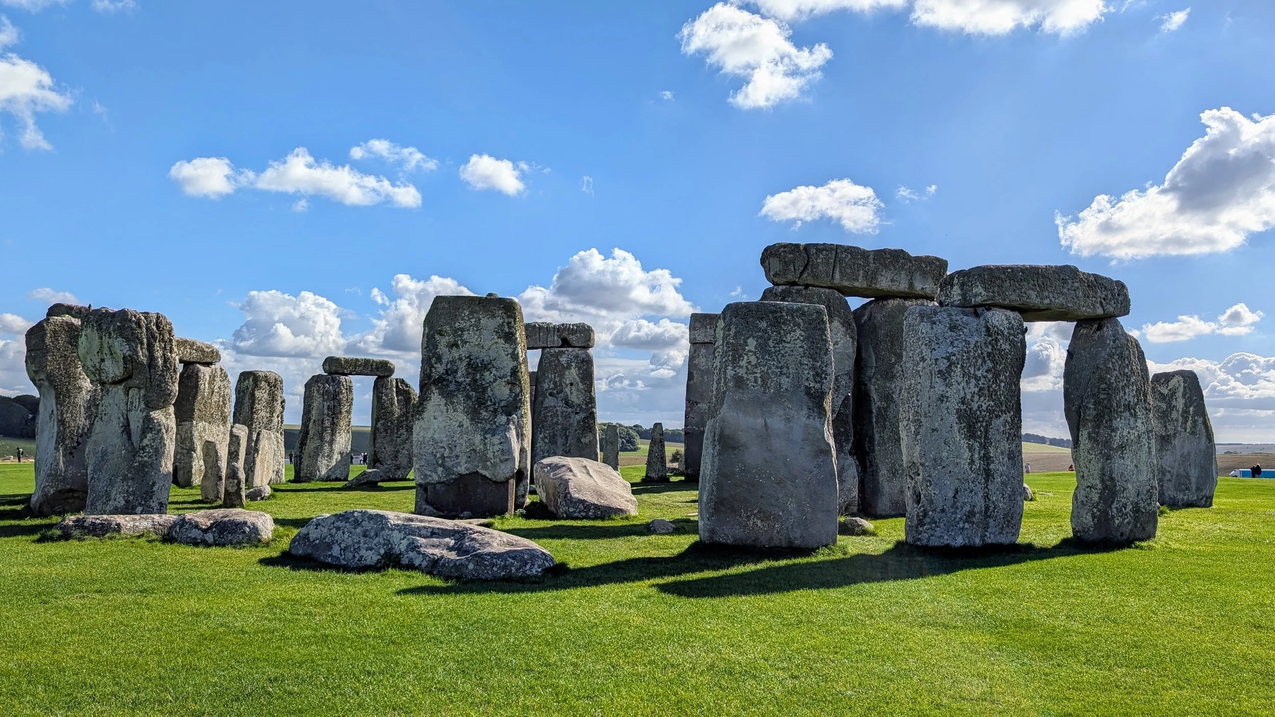 Ancient stone circle at Stonehenge under a partly cloudy blue sky.
