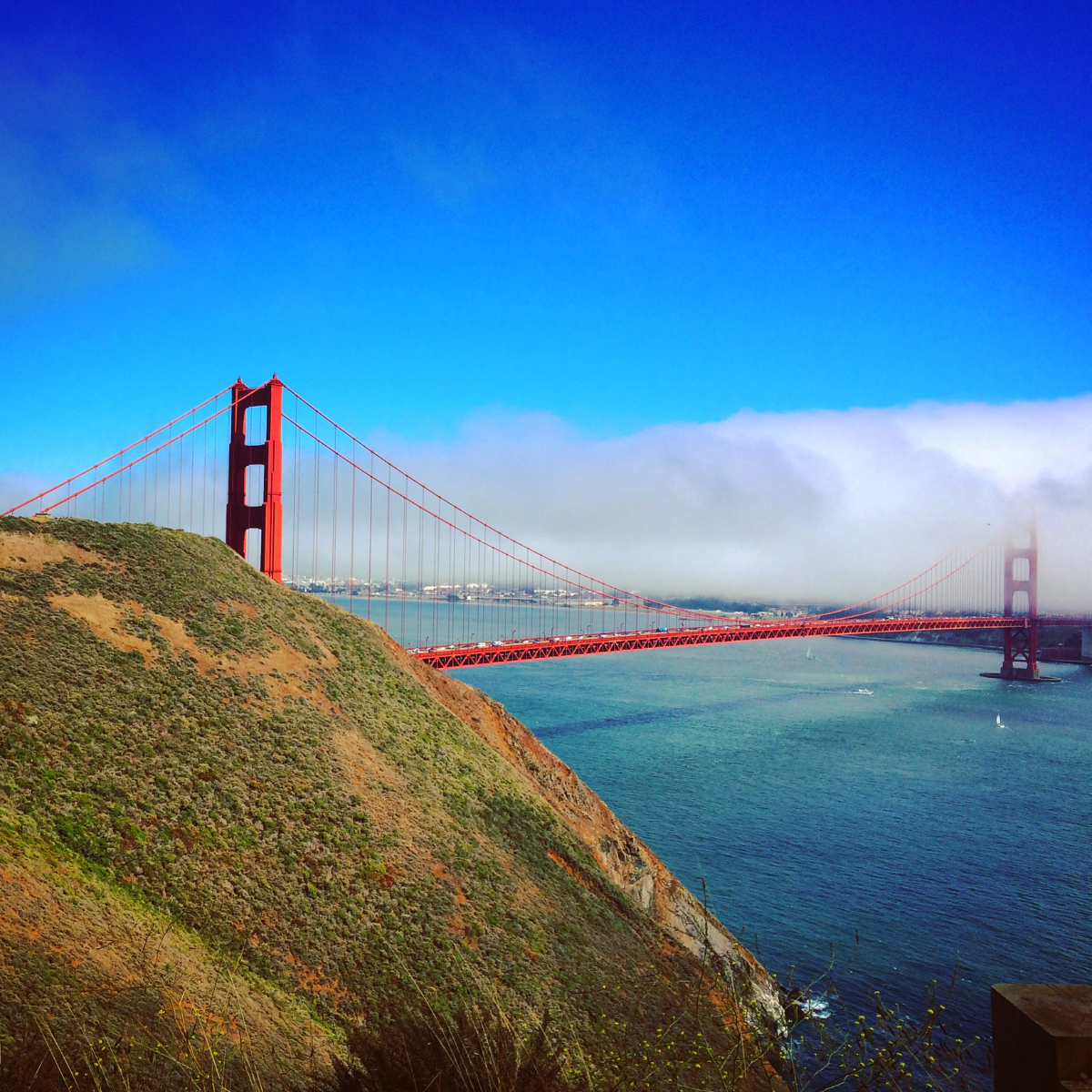 The Golden Gate Bridge in San Francisco, California, with fog partially covering the bridge's towers, surrounded by water and hills.
