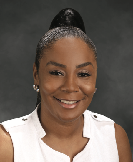 Close-up portrait of a smiling African American woman with a high ponytail, wearing a white sleeveless top and pearl earrings, against a dark background.