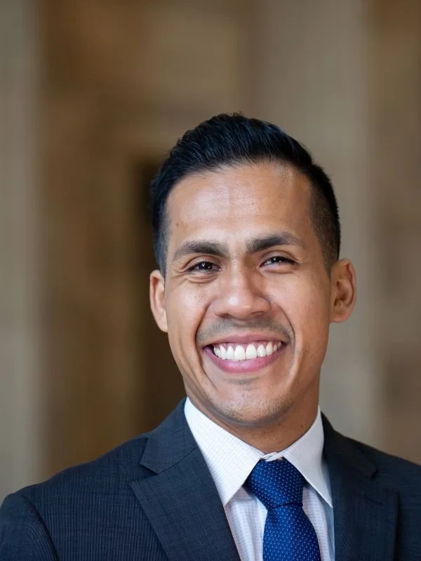 A smiling man in a suit and tie posing for a portrait indoors.
