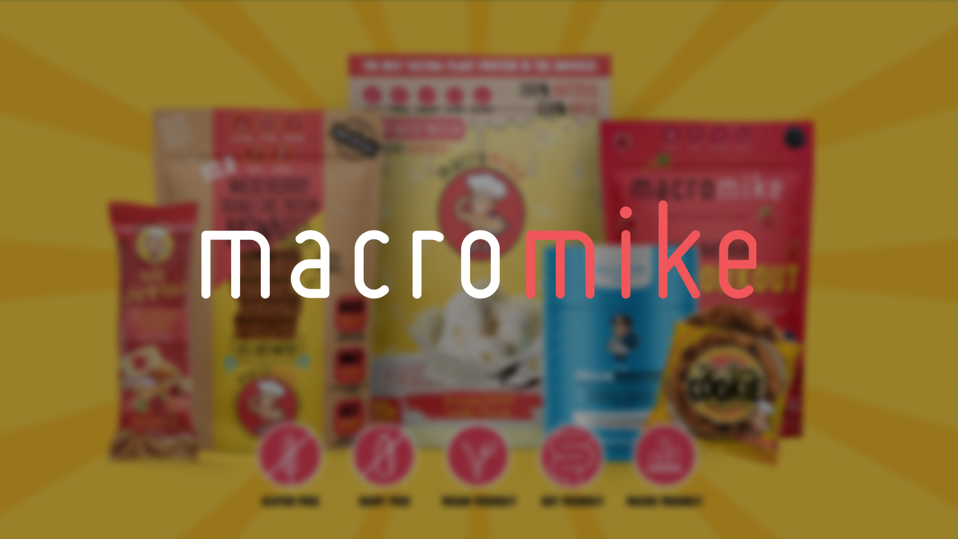 A colorful assortment of snack and food packages with a yellow background radiating outward, featuring the Macro Mike logo in the foreground.