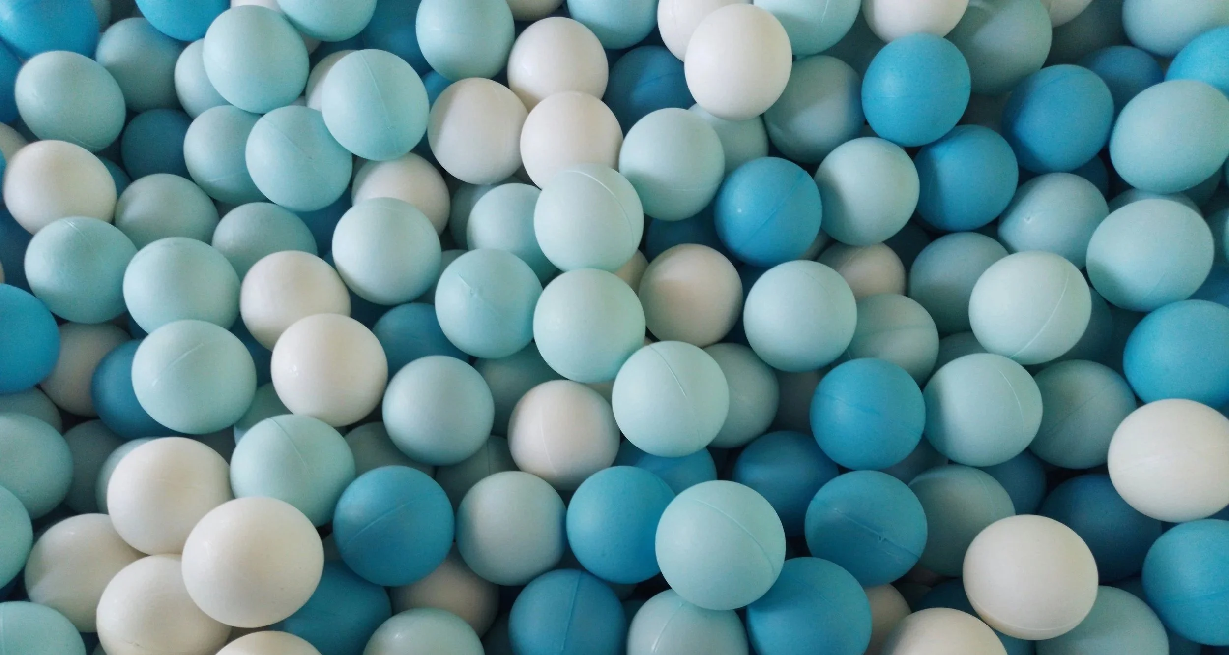 A close-up image of numerous light blue, white, and darker blue plastic balls, typically found in a ball pit.