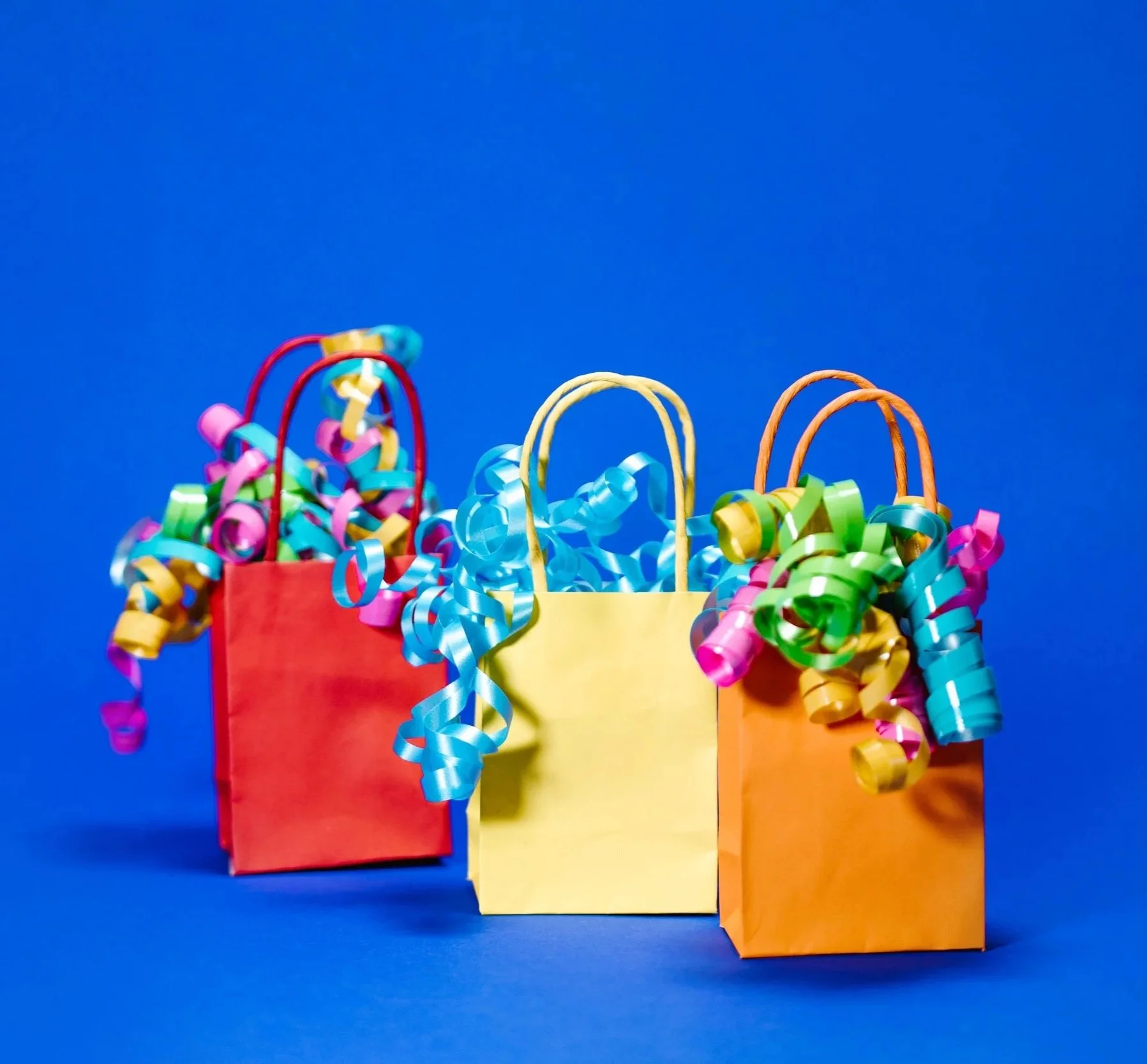 Three colorful gift bags with curling ribbons against a blue background.