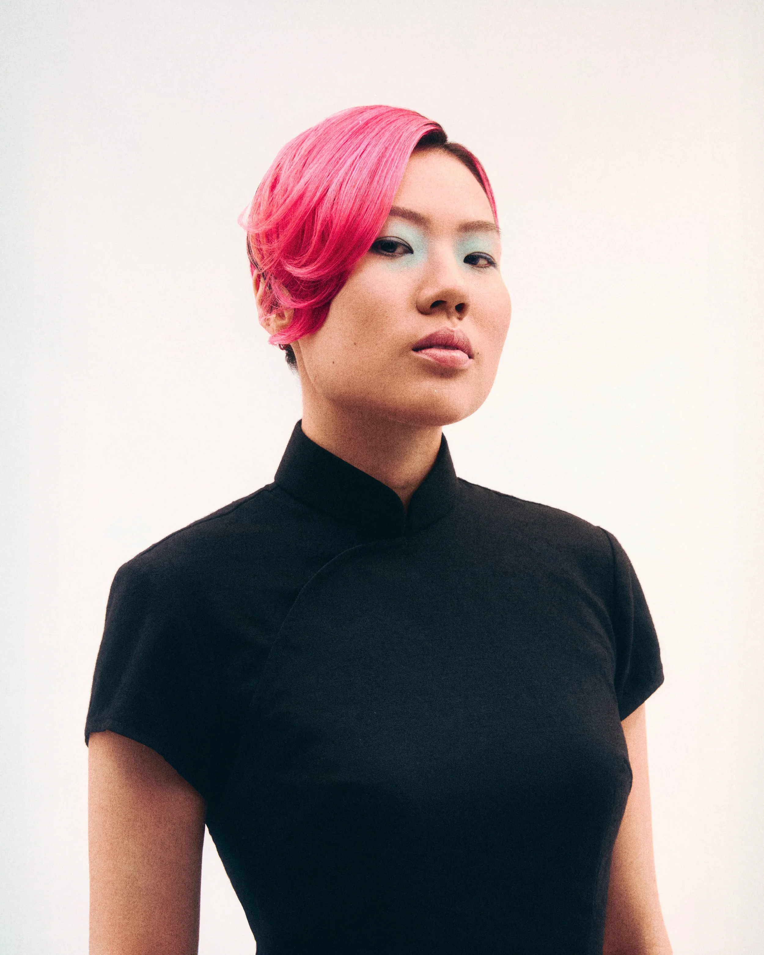 Close-up of a woman with short pink hair wearing a black top.