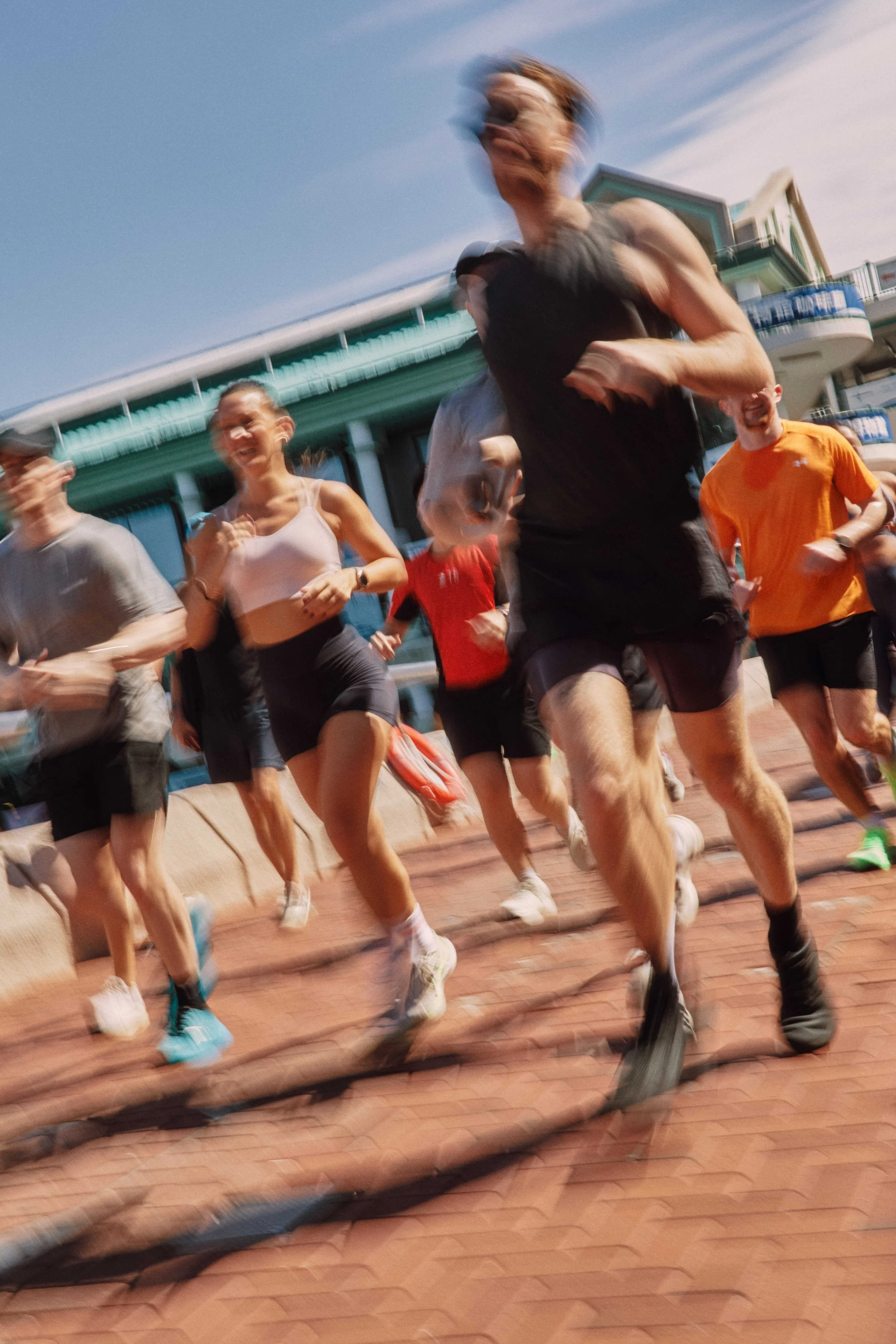 People running outdoors on a sunny day, with a building and a clear blue sky in the background.