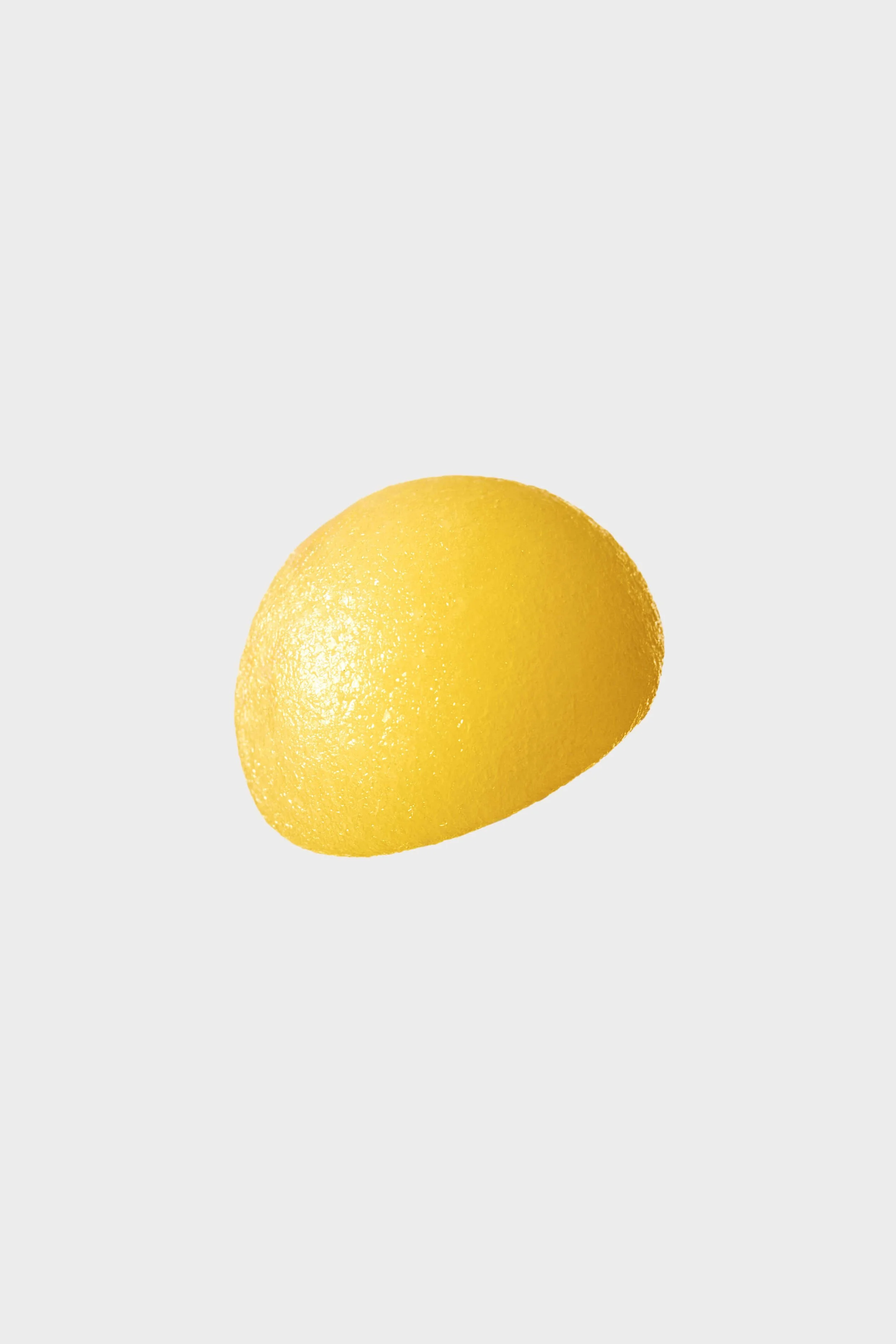 Close-up of a bright yellow lemon against a plain light gray background.