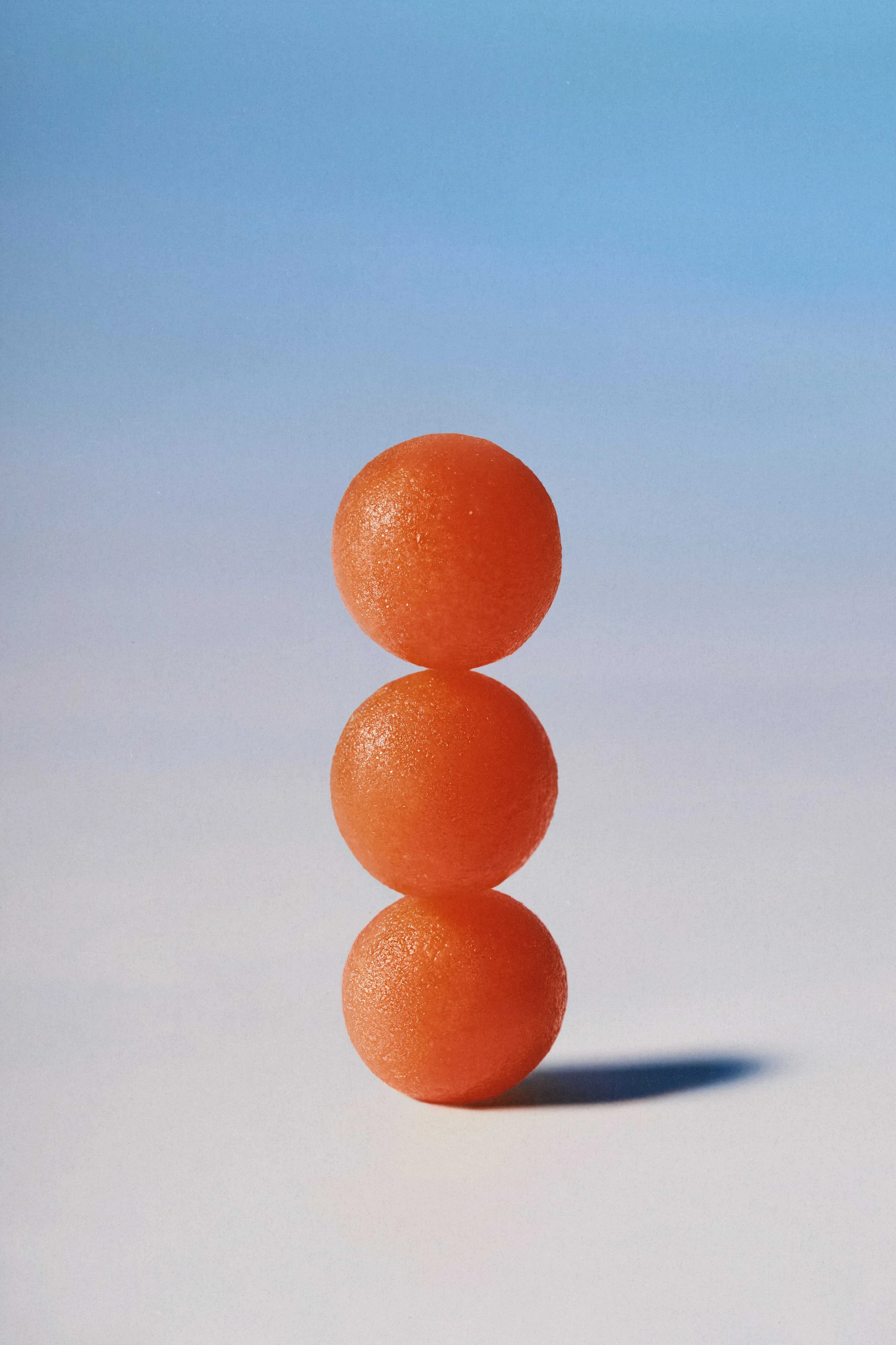 Five orange spherical objects stacked vertically with a blue sky background and a shadow cast on the ground.