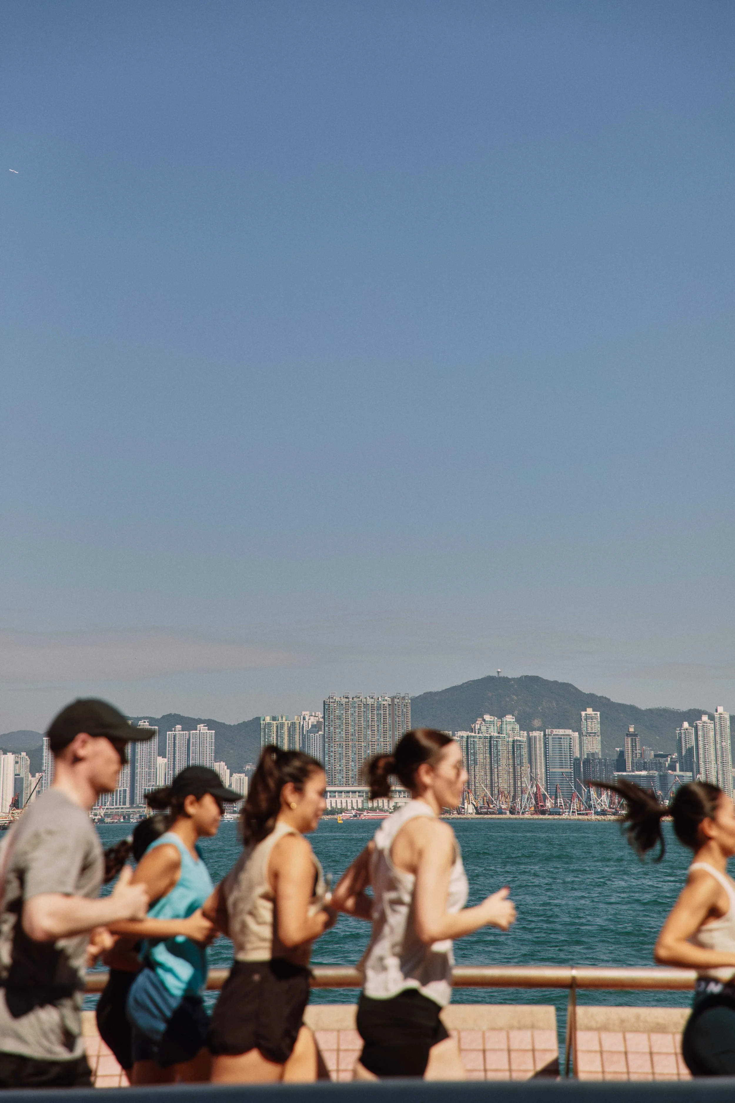 People jogging along a waterfront with a city skyline and mountain in the background.