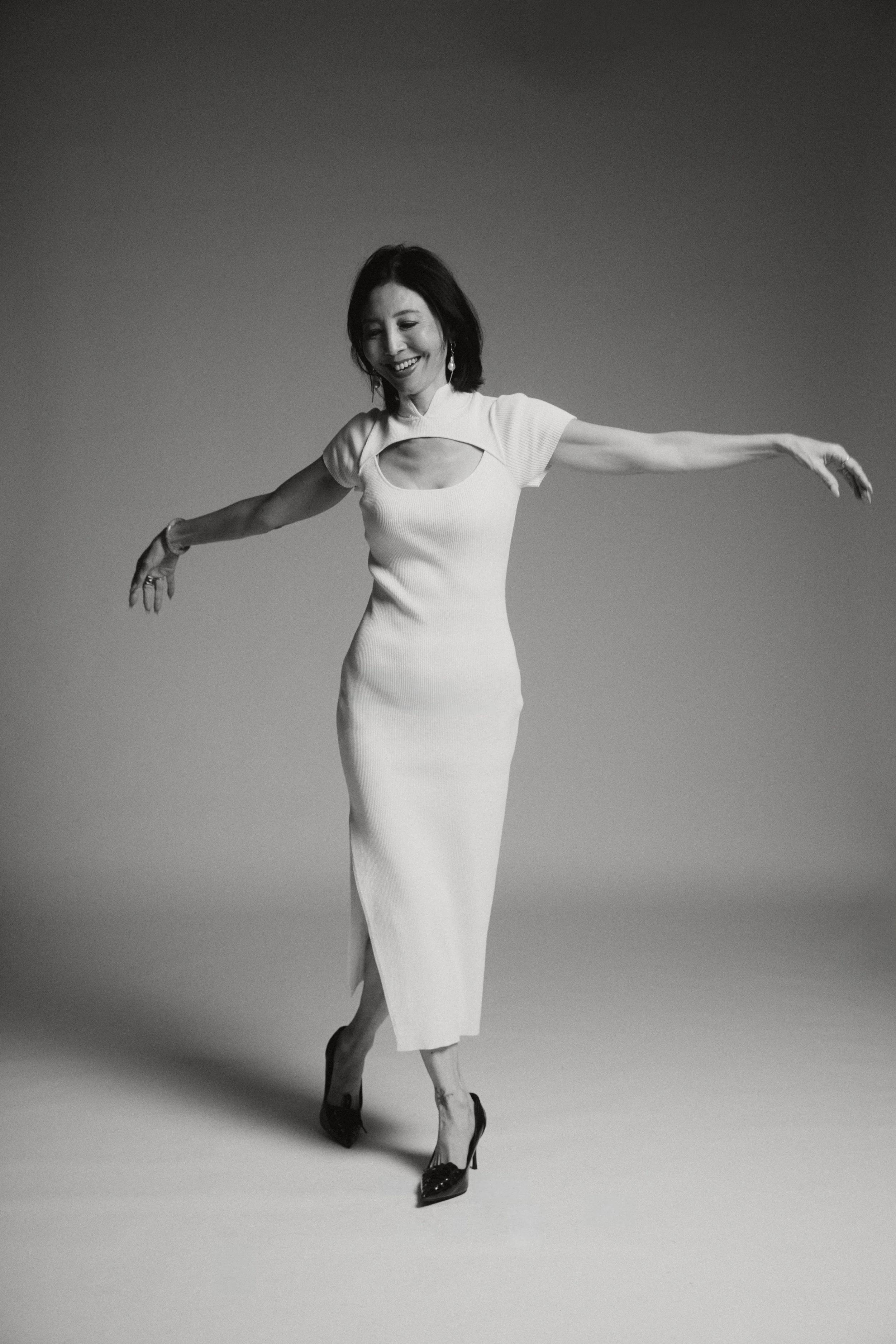 Black and white photo of a woman in a elegant dress with arms open, smiling, with a gradient background.