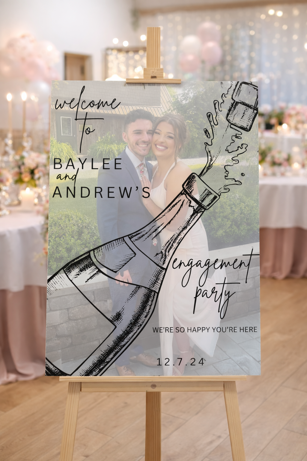 Wedding reception sign with a photo of a smiling couple, overlayed with a graphic of a champagne bottle spraying, and text reading "Welcome to Baylee and Andrew's engagement party," with the date 12.7.24 and the message "We're so happy you're here."