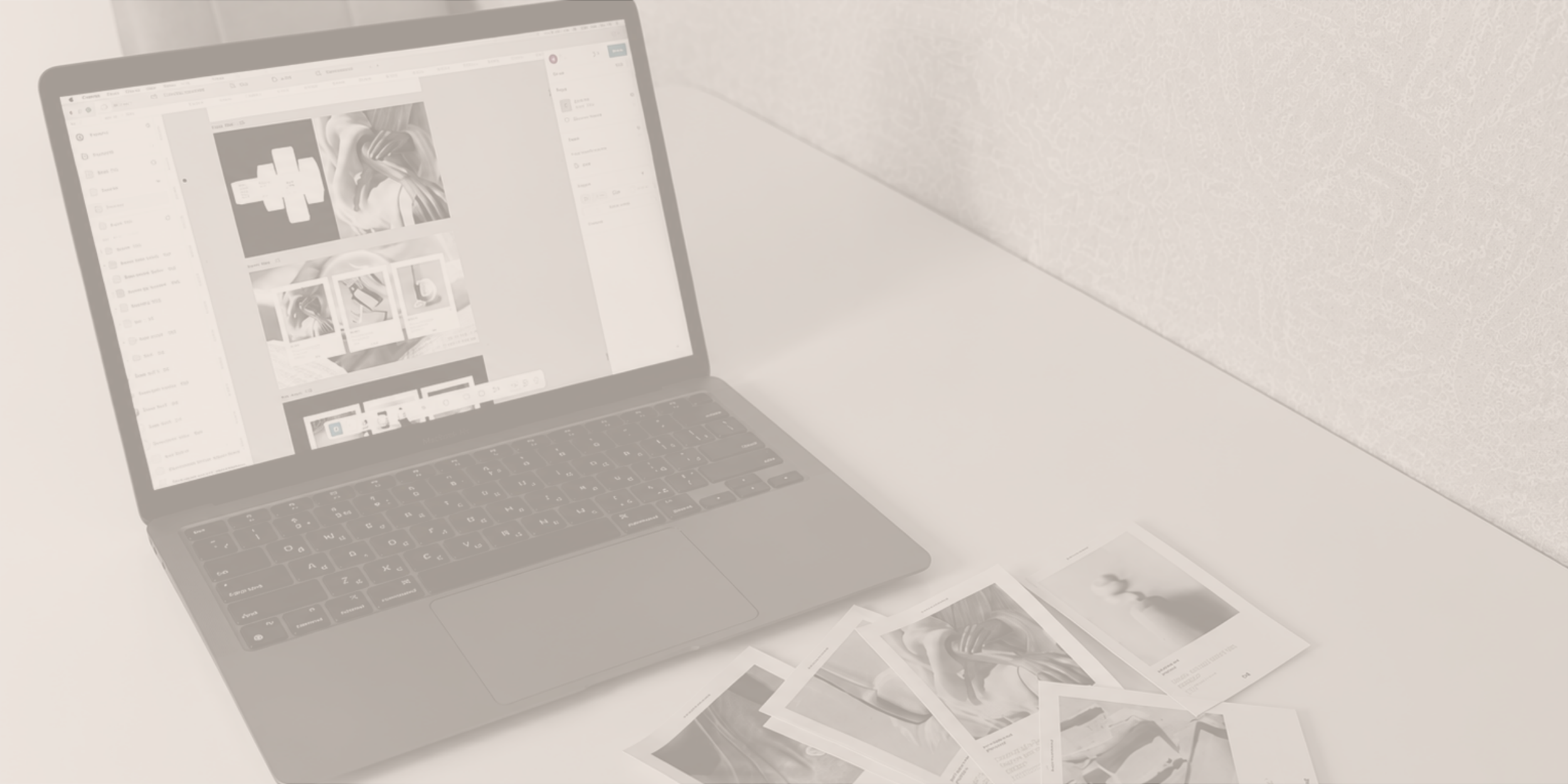 A laptop on a white desk with printed photographs spread out beside it, showing a digital workspace with design images on the screen.