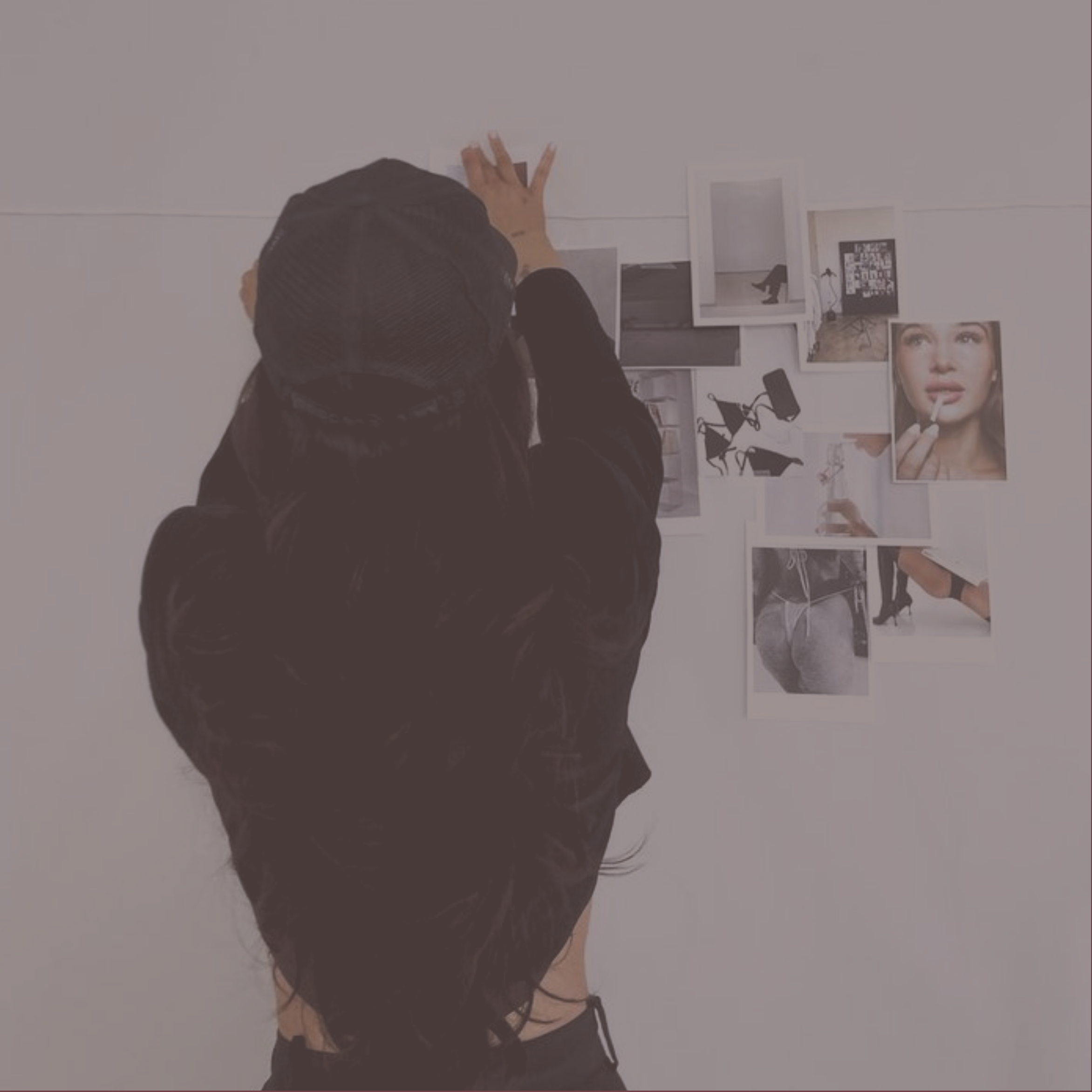 A woman with black hair in a bun, wearing a black top, taking a photo of a white wall in a gallery or art space with her phone.