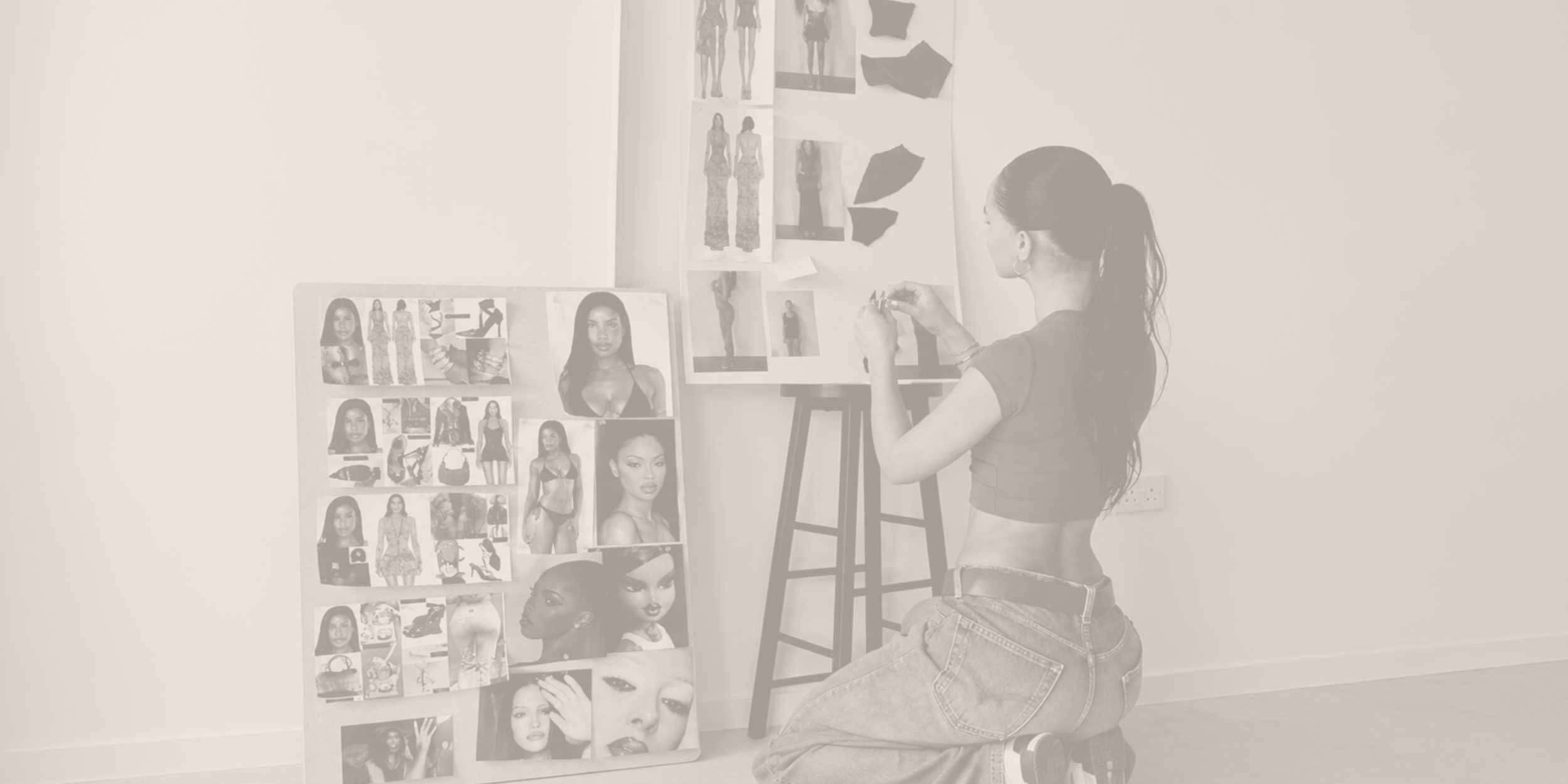 A woman kneeling on the floor arranging photos of models on a collage board in a room with white walls.