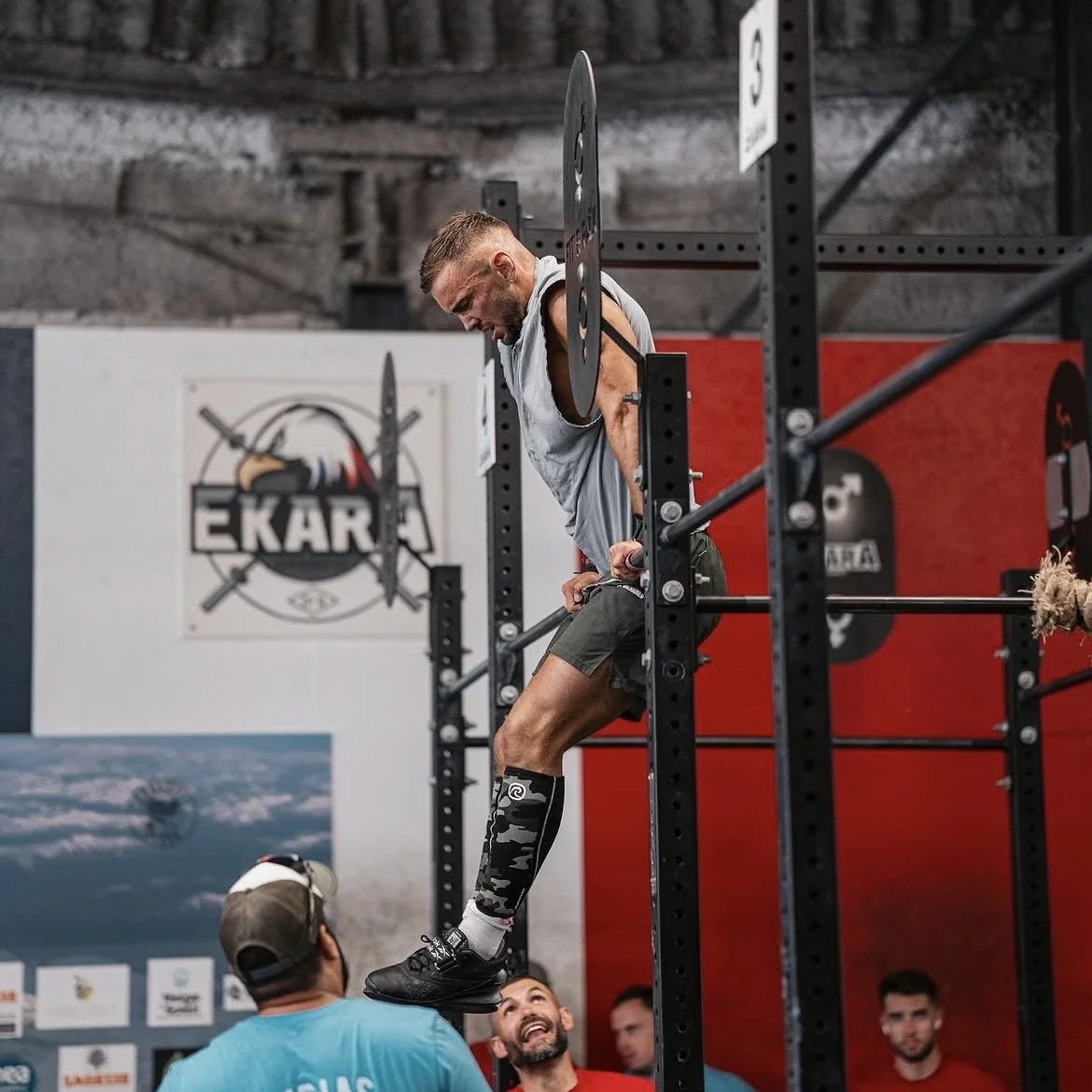 Un homme en train de faire des exercices de musculation sur une barre fixe dans une salle de sport, avec d'autres personnes regardant.
