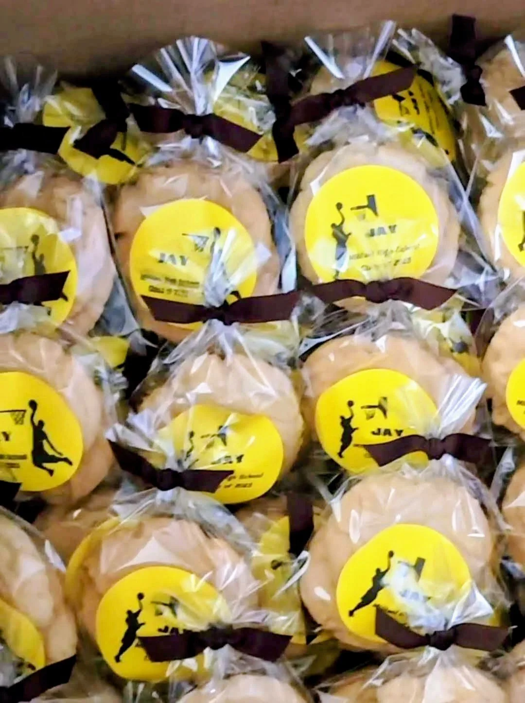 Multiple wrapped cookies with yellow labels and brown ribbons, stacked in a box.