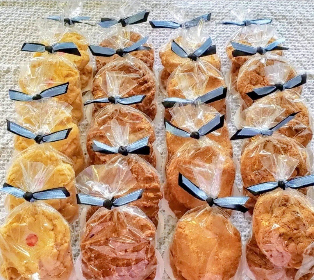 Cookies individually wrapped in clear plastic bags tied with black and blue ribbons, arranged on a textured white surface.