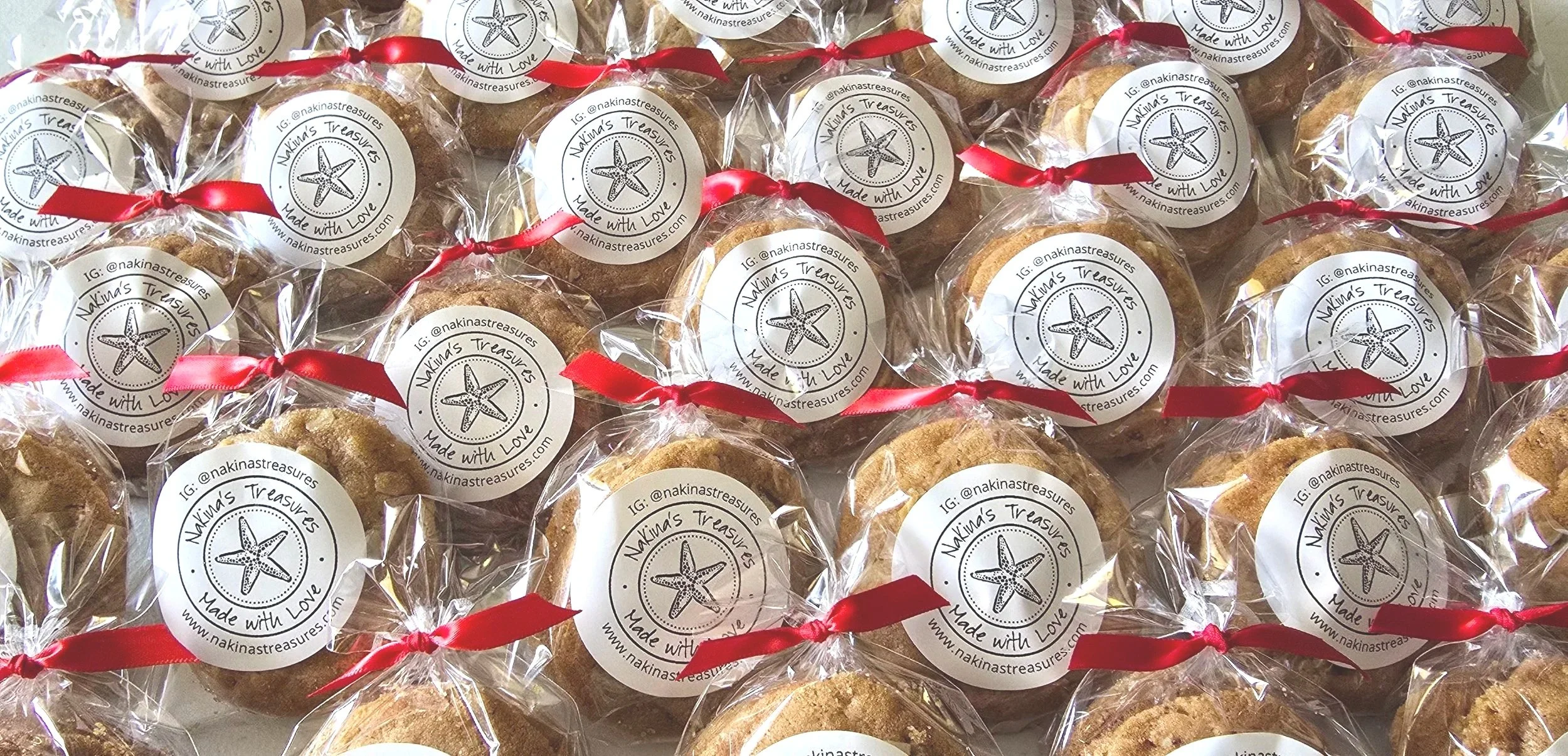 A collection of homemade cookies individually wrapped in clear plastic with red ribbons, each with a round label that reads 'Nakin's Treasures, Made with Love' and features a starfish graphic.