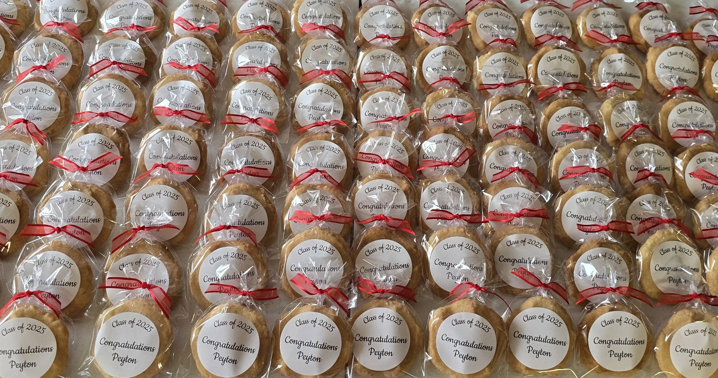 Numerous cookies wrapped in clear plastic with circular labels that read 'Class of 2025 Congratulations Peyton' tied with red ribbon.