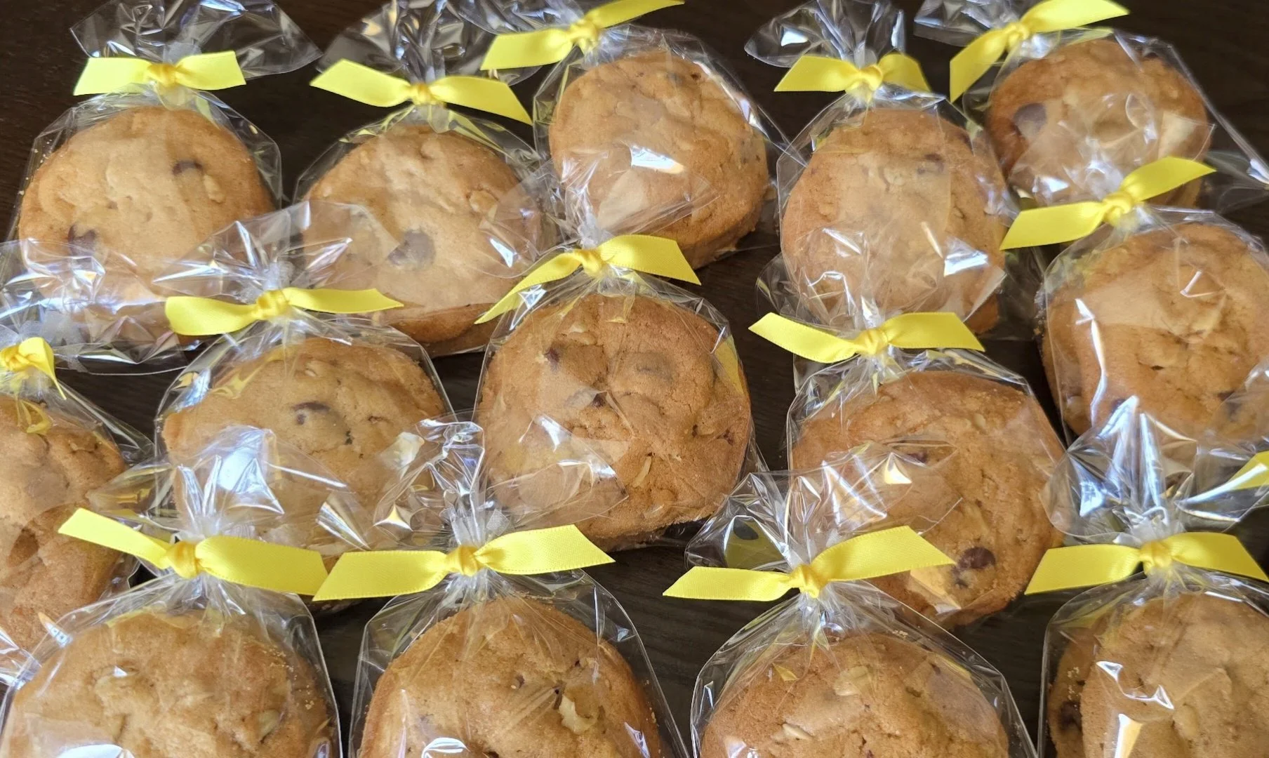 Several cookies wrapped in clear plastic and tied with yellow ribbons are arranged on a dark wooden surface.