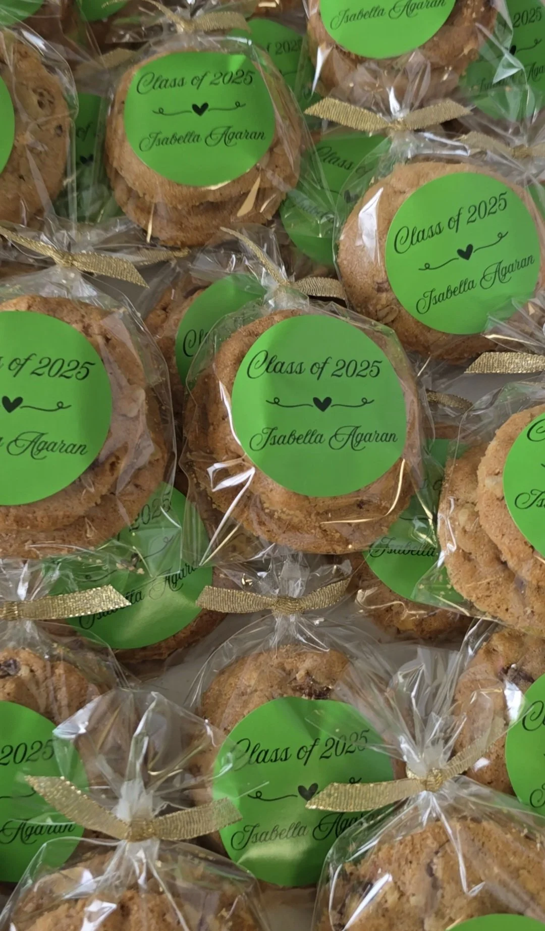 Cookies wrapped in clear plastic with a green label that reads 'Class of 2025 Isabella Agaran,' tied with a gold ribbon.
