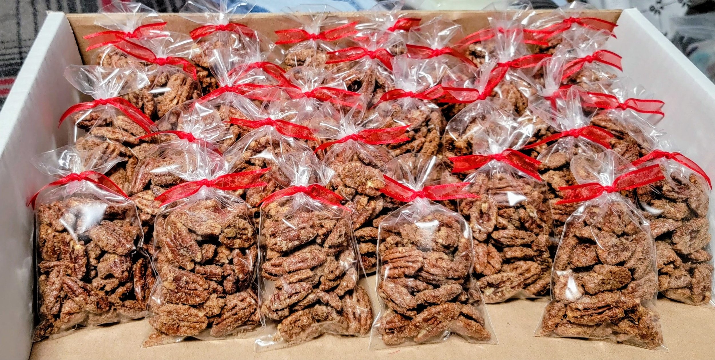 A large box filled with individually wrapped pecan pralines tied with red ribbons.