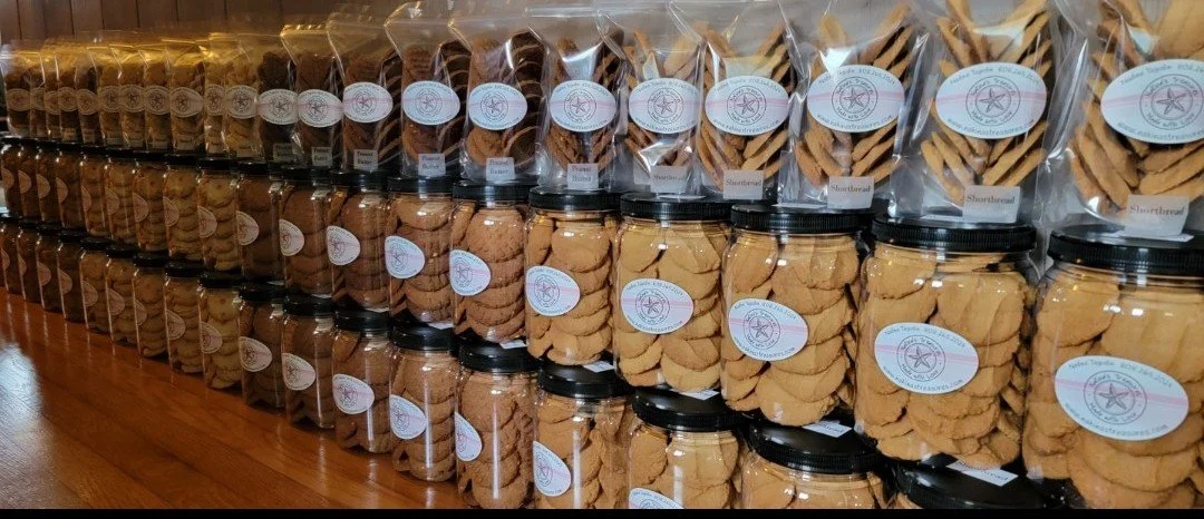 Rows of jars and clear plastic bags filled with various types of cookies on wooden shelves.