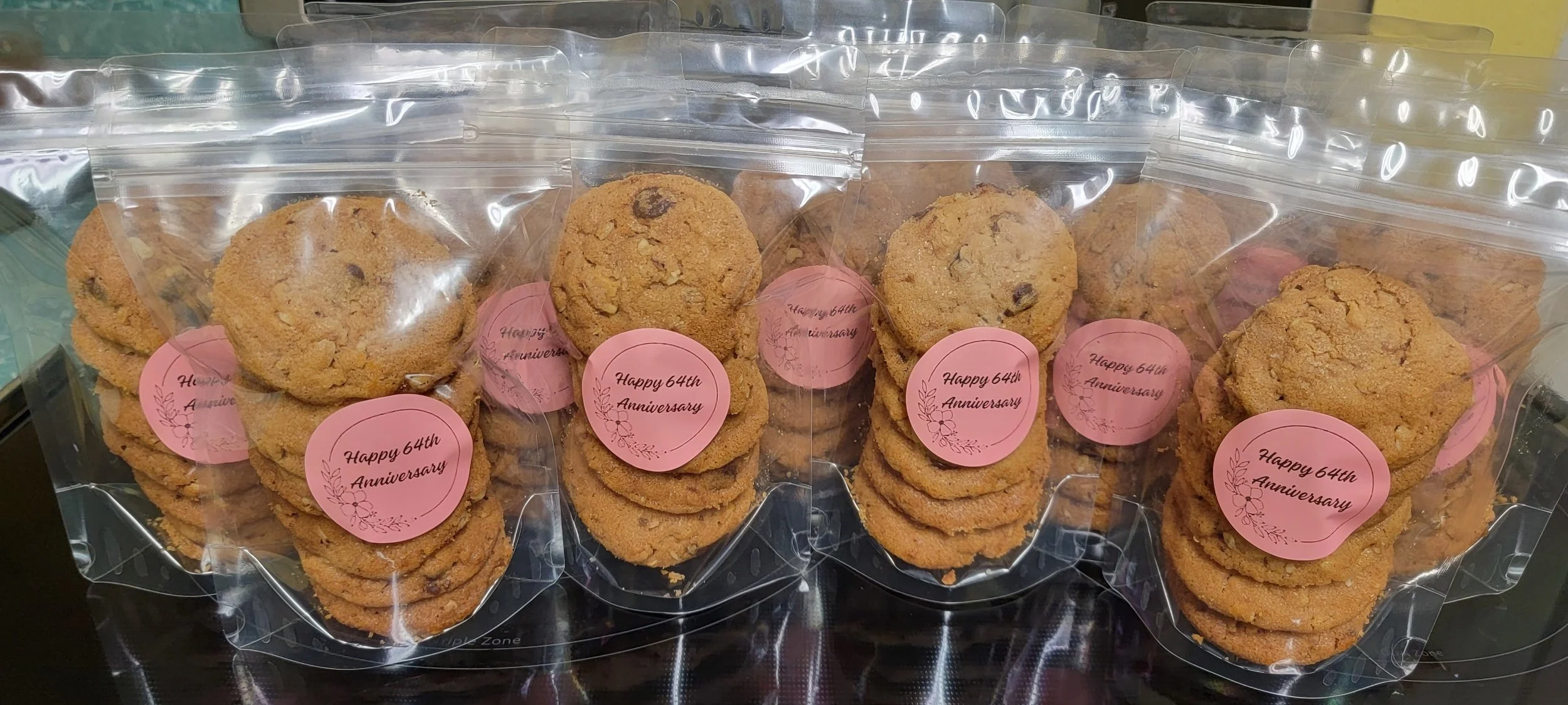 Multiple packages of chocolate chip cookies with pink stickers that read "Happy 64th Anniversary."
