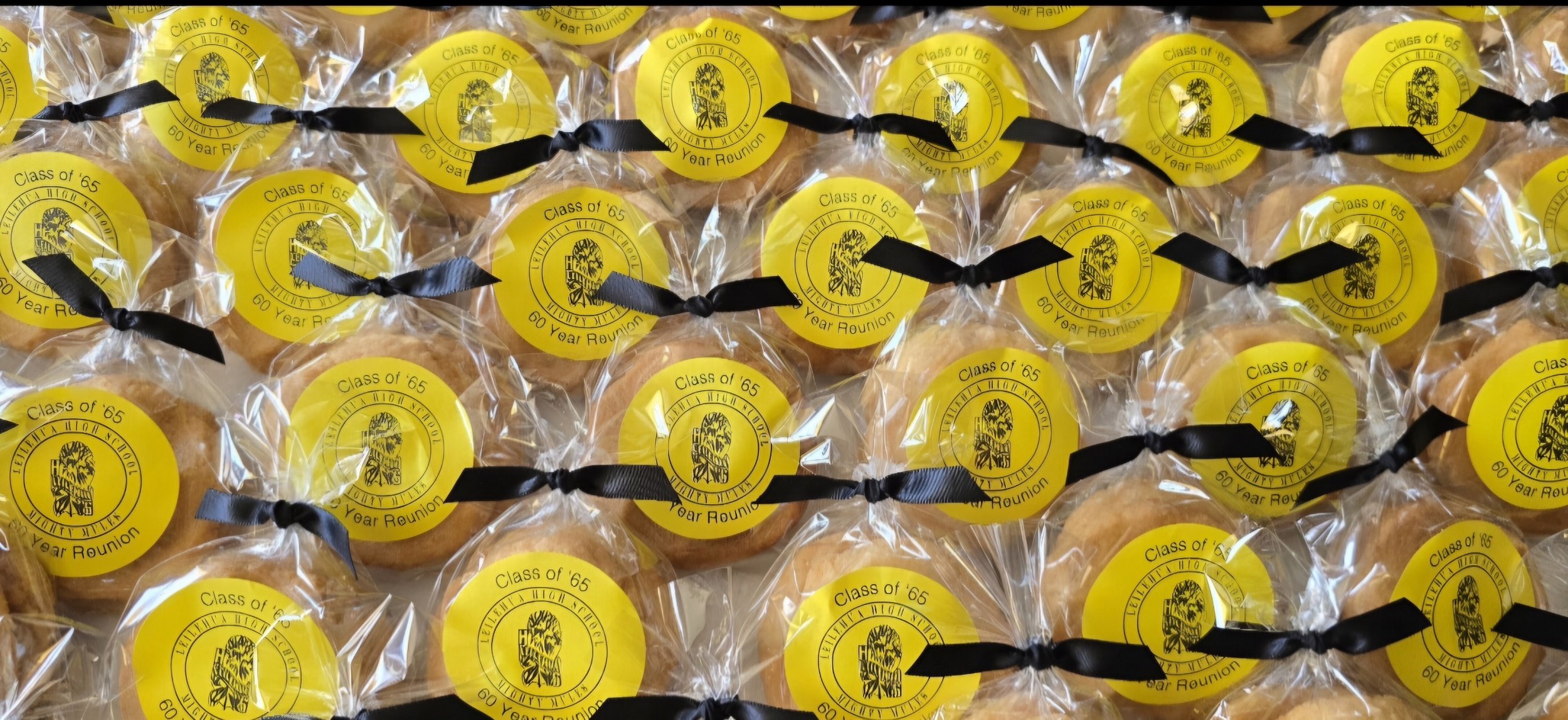 Individual cookies wrapped in clear plastic with yellow labels that say 'Class of '65 60 Year Reunion' and black ribbons.