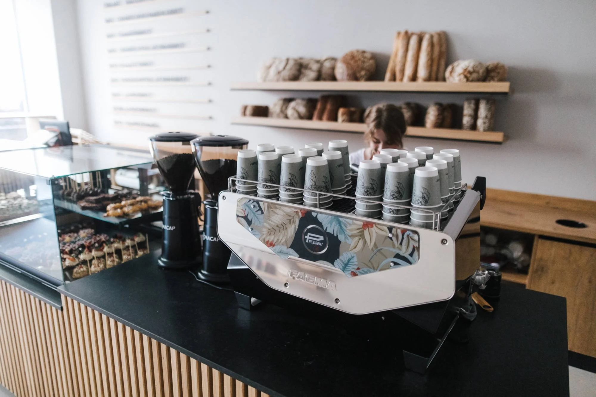 Eine Kaffeestation mit Kaffeebechern, Kaffeemaschinen, Torten und Keksen in einem Café.