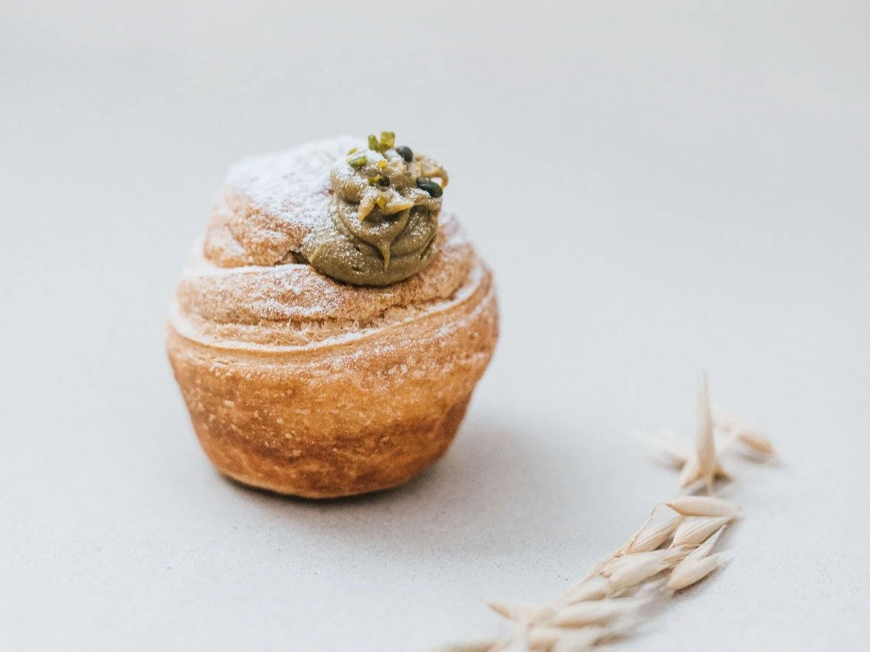 Ein Cupcake mit grünem Zuckerguss und Pistazien, bestäubt mit Puderzucker, auf weißem Hintergrund mit Weizenähren