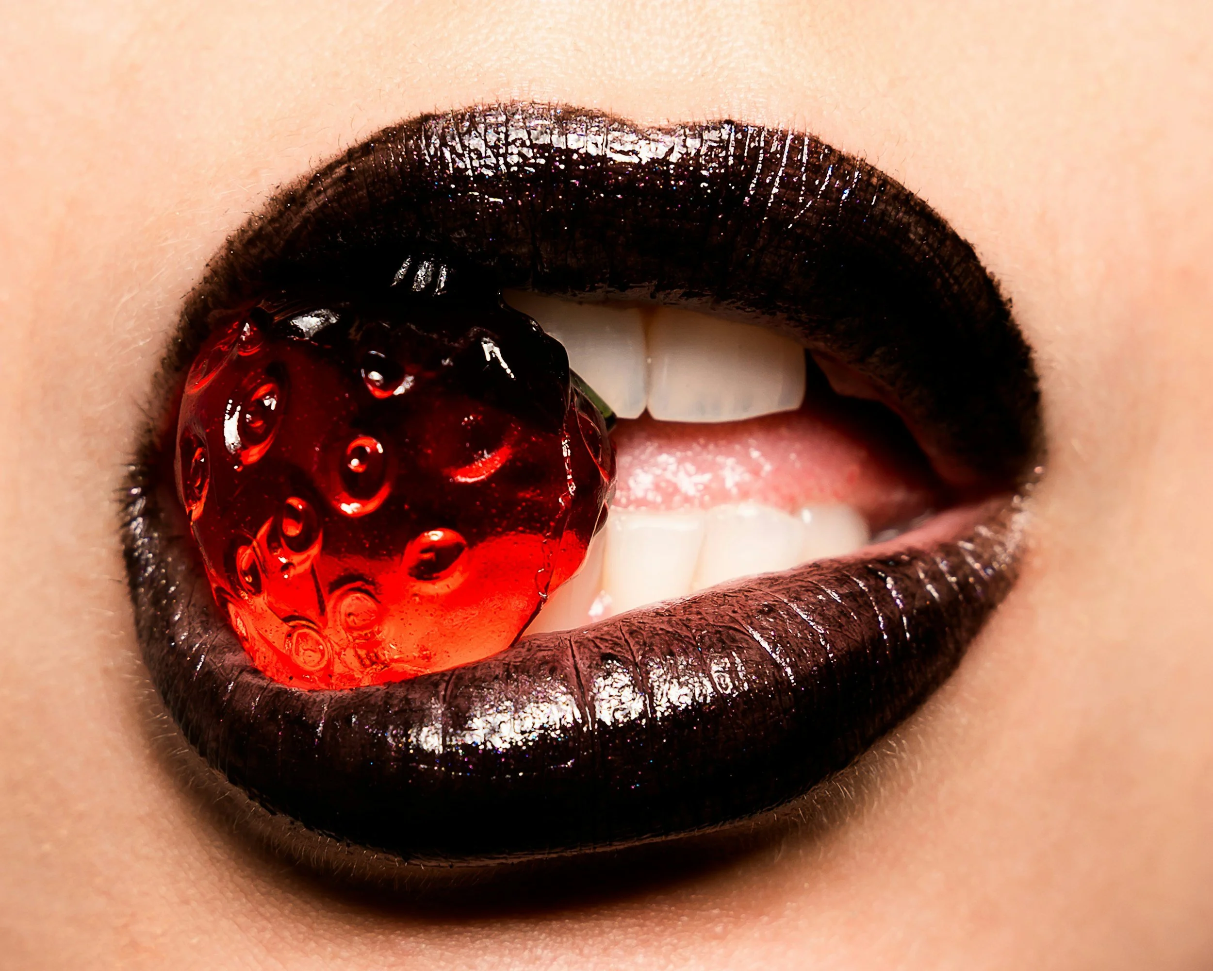 Close-up of a person's mouth with dark lipstick, featuring black lips and a cherry placed on the lower lip.