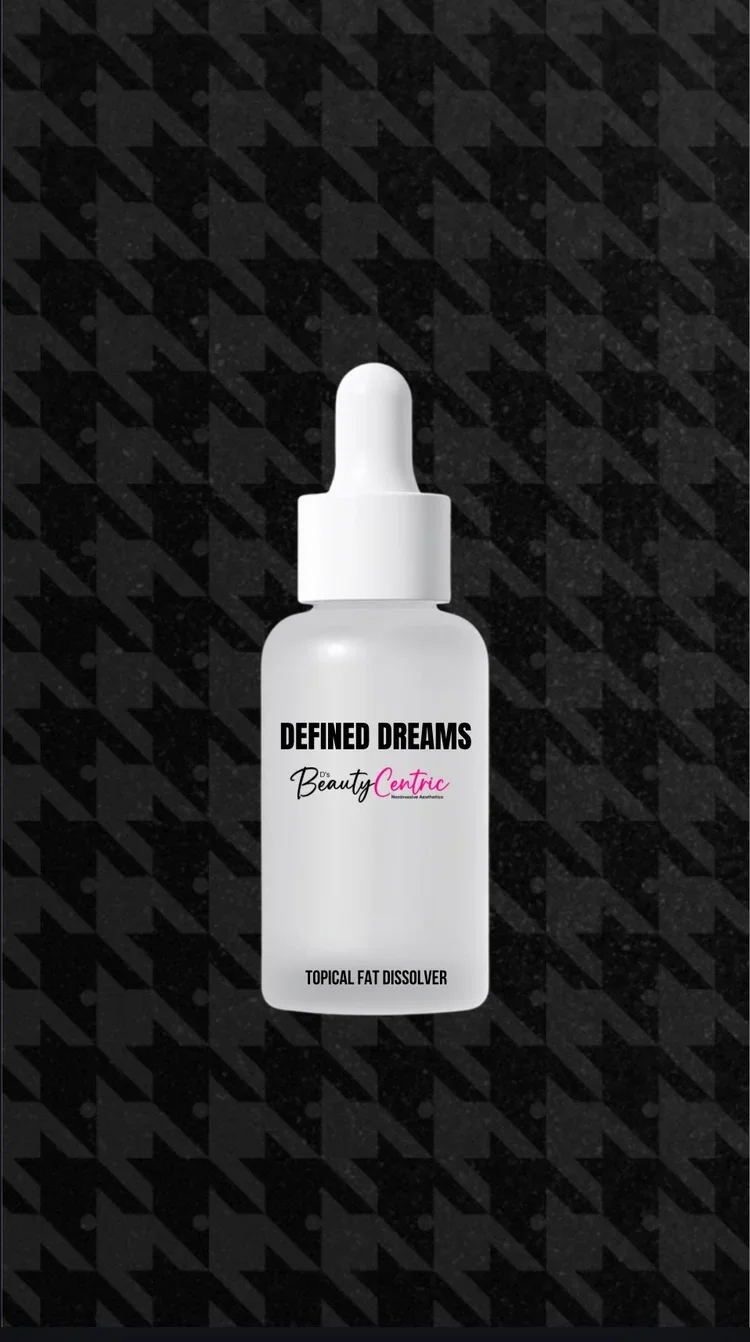 A white bottle with a dropper cap labeled 'DEFINED DREAMS Topical Fat Dissolver' from D's Beauty Centric, set against a black background with a houndstooth pattern.