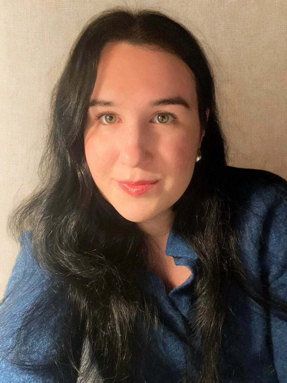 Ragazza con capelli lunghi e neri, indossa una camicia blu, sfondo neutro.