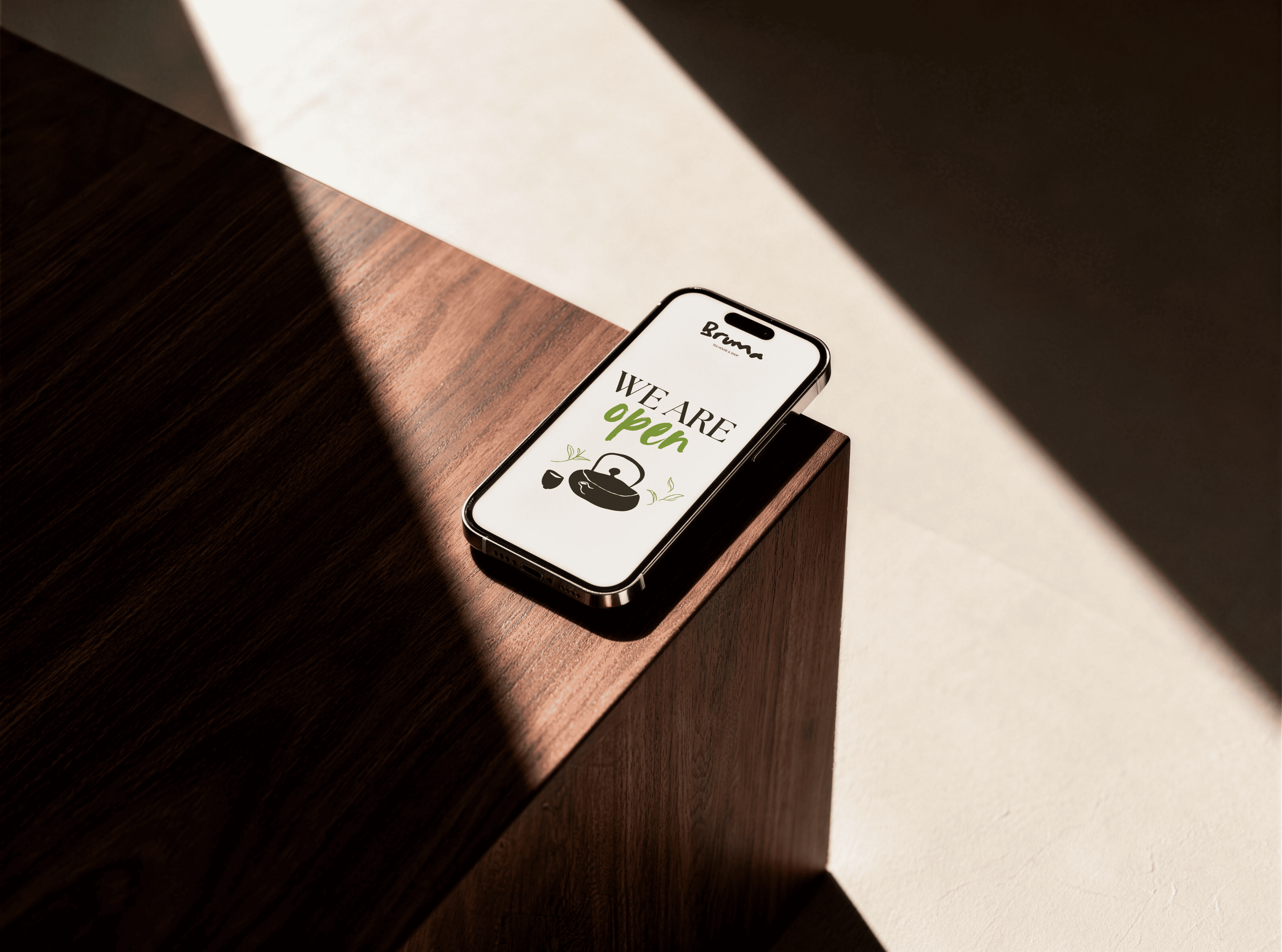Smartphone con schermo che dice "We are open" in esposizione su un tavolo di legno, con luce naturale che crea un'ombra e un contrasto tra la zona illuminata e quella in ombra.