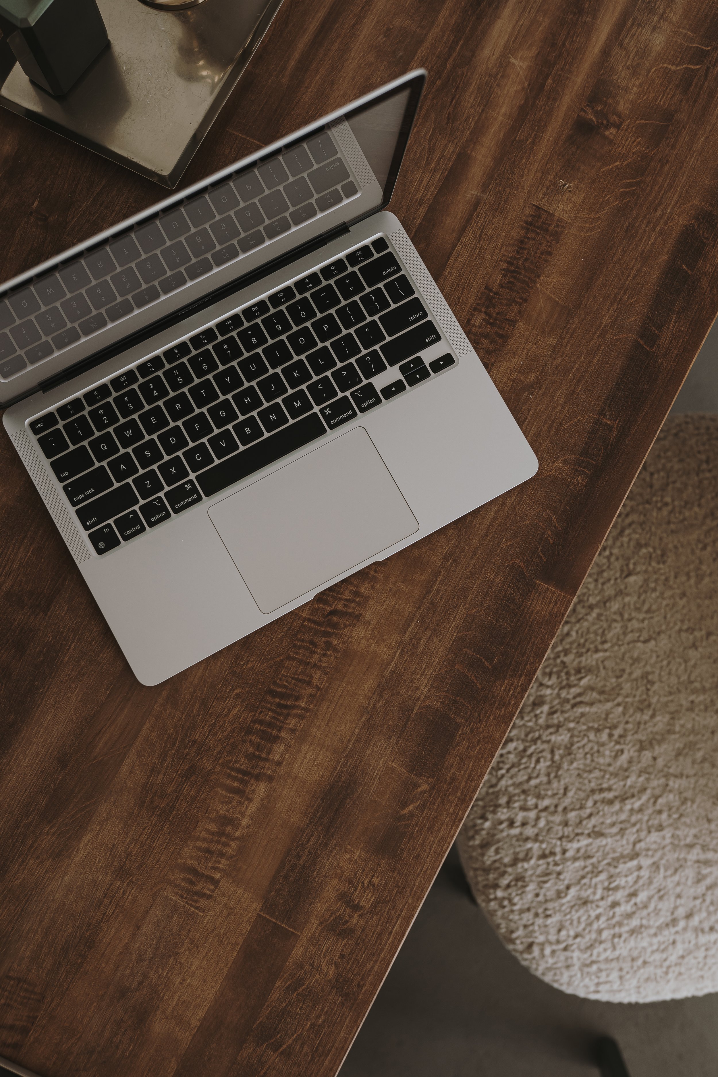 Un computer MacBook sopra un tavolo di legno, con uno schermo aperto e la tastiera visibile, e un sottostante tappeto beige.