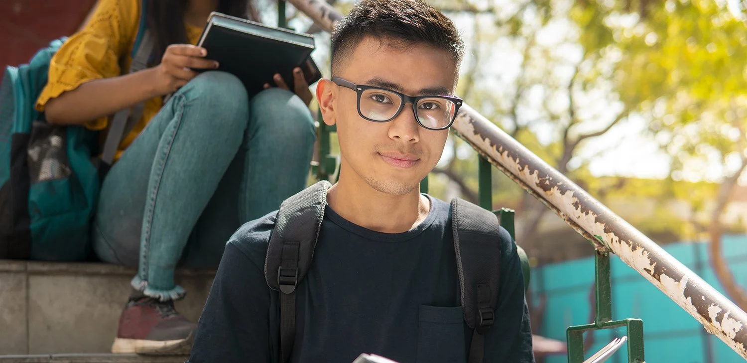 A young, male student of Directions to Diploma sitting outside in the bleachers. (hero image)