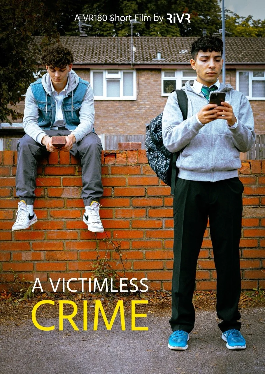 Two young males standing outside in front of a brick wall, both looking at their phones. One is sitting on the wall wearing sneakers, and the other is standing wearing sneakers and a backpack. Text overlay: "A VR180 Short Film by RiVR. A Victimless Crime."